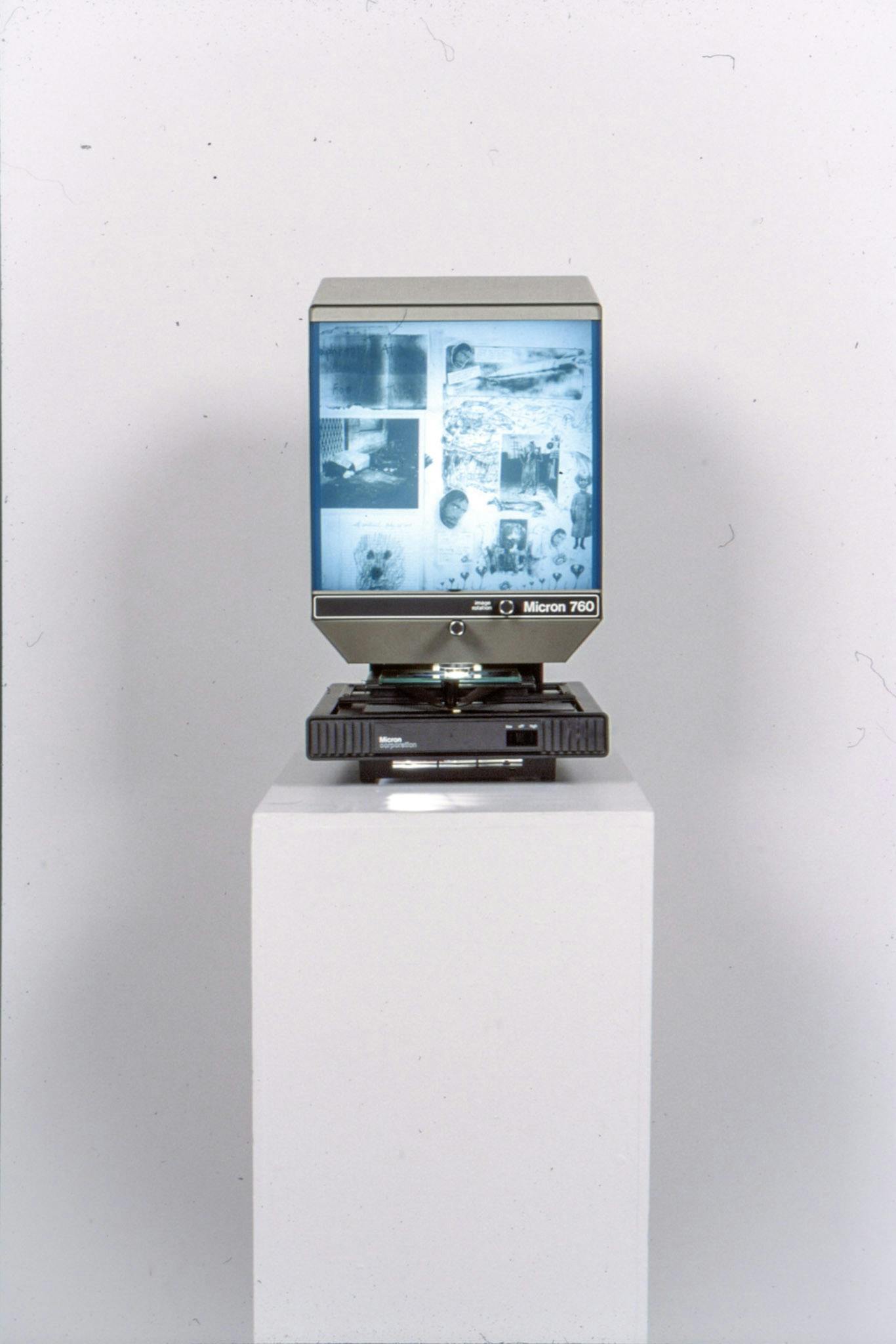 An installation image of artworks in a gallery. A machine named Micron 760, which looks like a desktop, is placed on a pedestal. The machine shows the collaged image of various drawings on its screen.