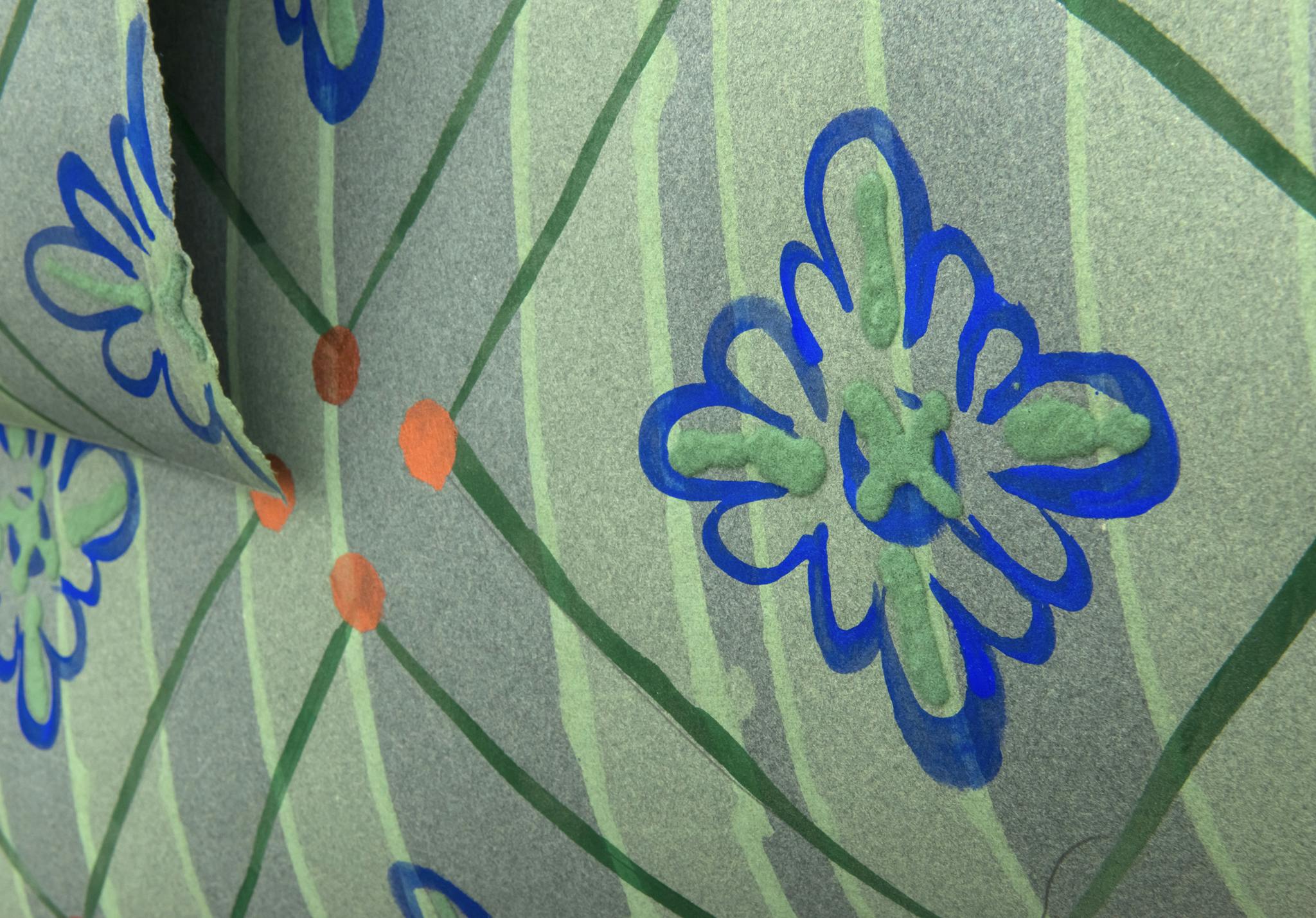 A close up section of hand-painted floral wallpaper. The wallpaper has a vertical green striped background with a pattern made up of blue flowers, green diamond shapes and orange circles overtop.