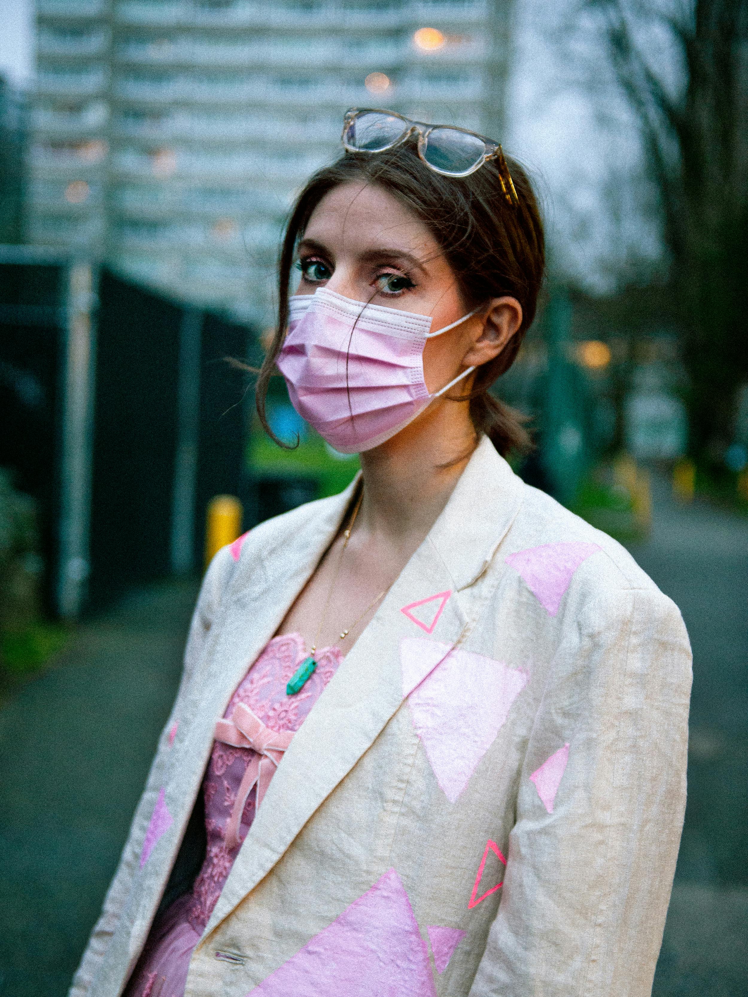 A portrait of Paige Smith. She is wearing a pink face mask and cream-coloured blazer with print triangles.