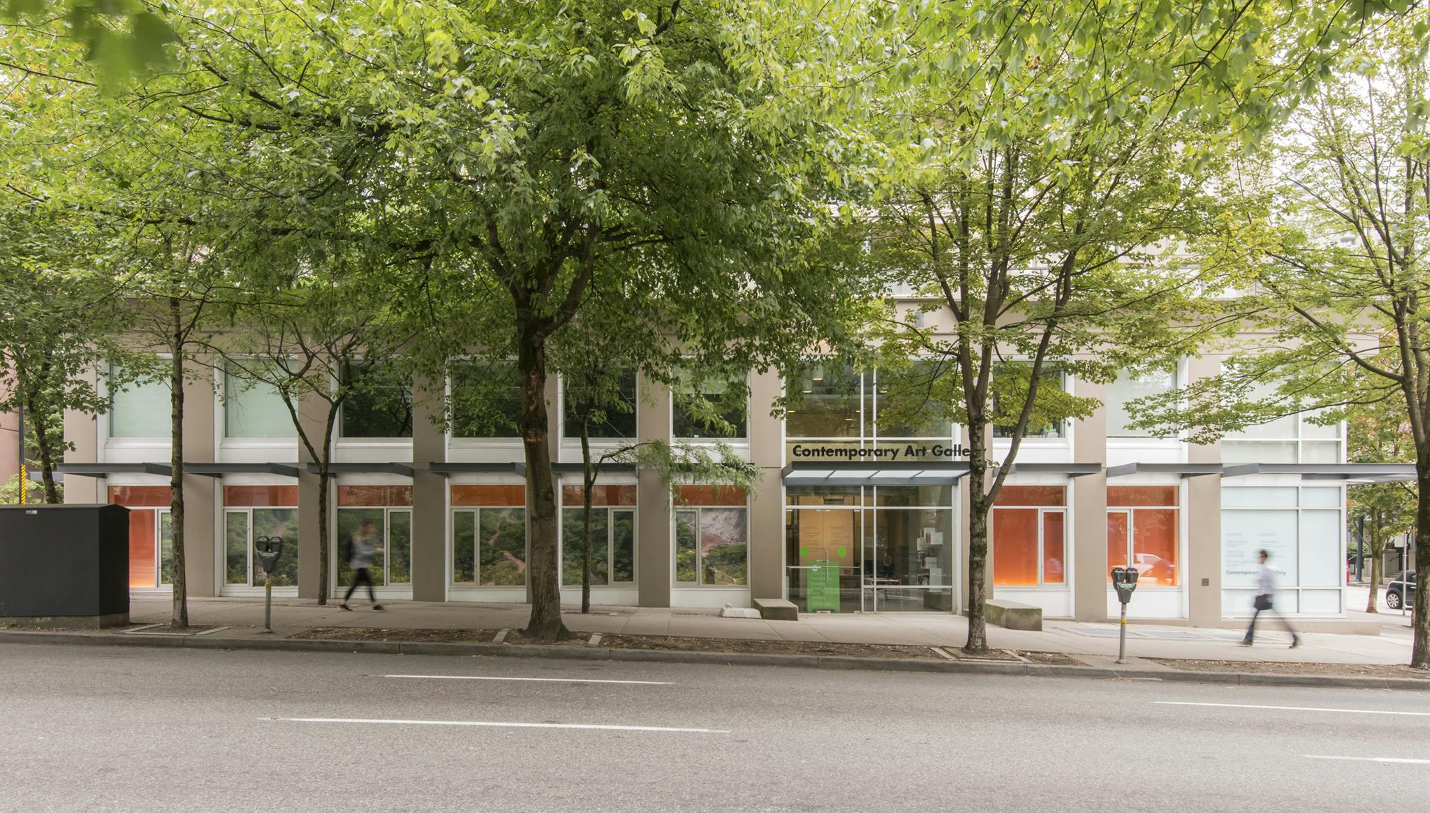 A wide shot image of the exterior of CAG. A panoramic photograph in vinyl of a rainforest landscape is installed across the façade windows over an orange background. 