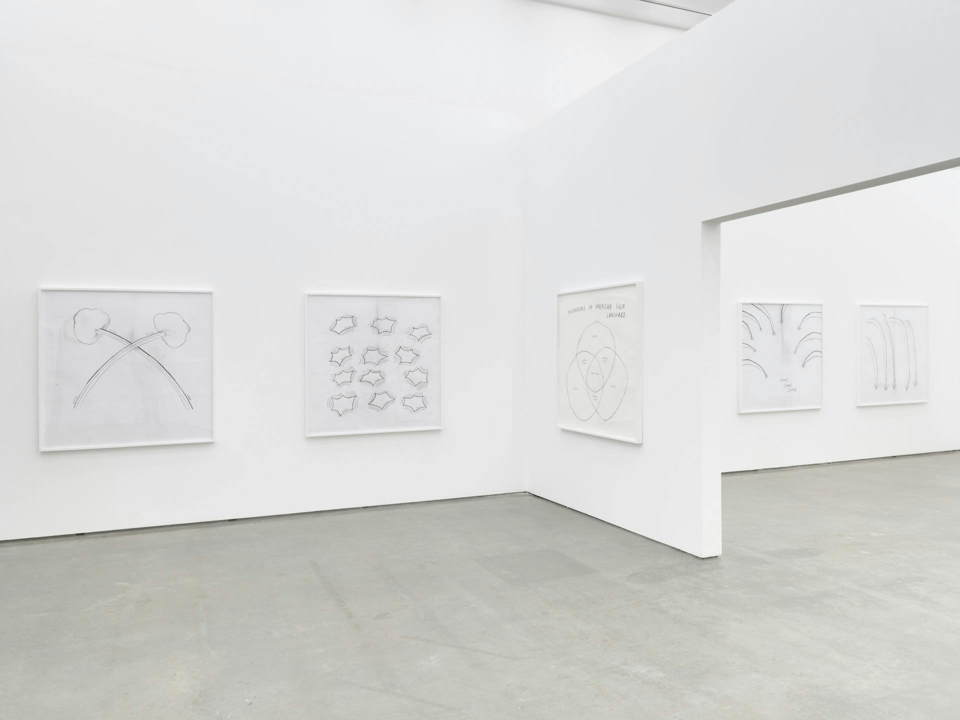 Four line drawings by Christine Sun Kim on a white wall bisected by a wall with an opening, which also has a drawing by Kim on it.