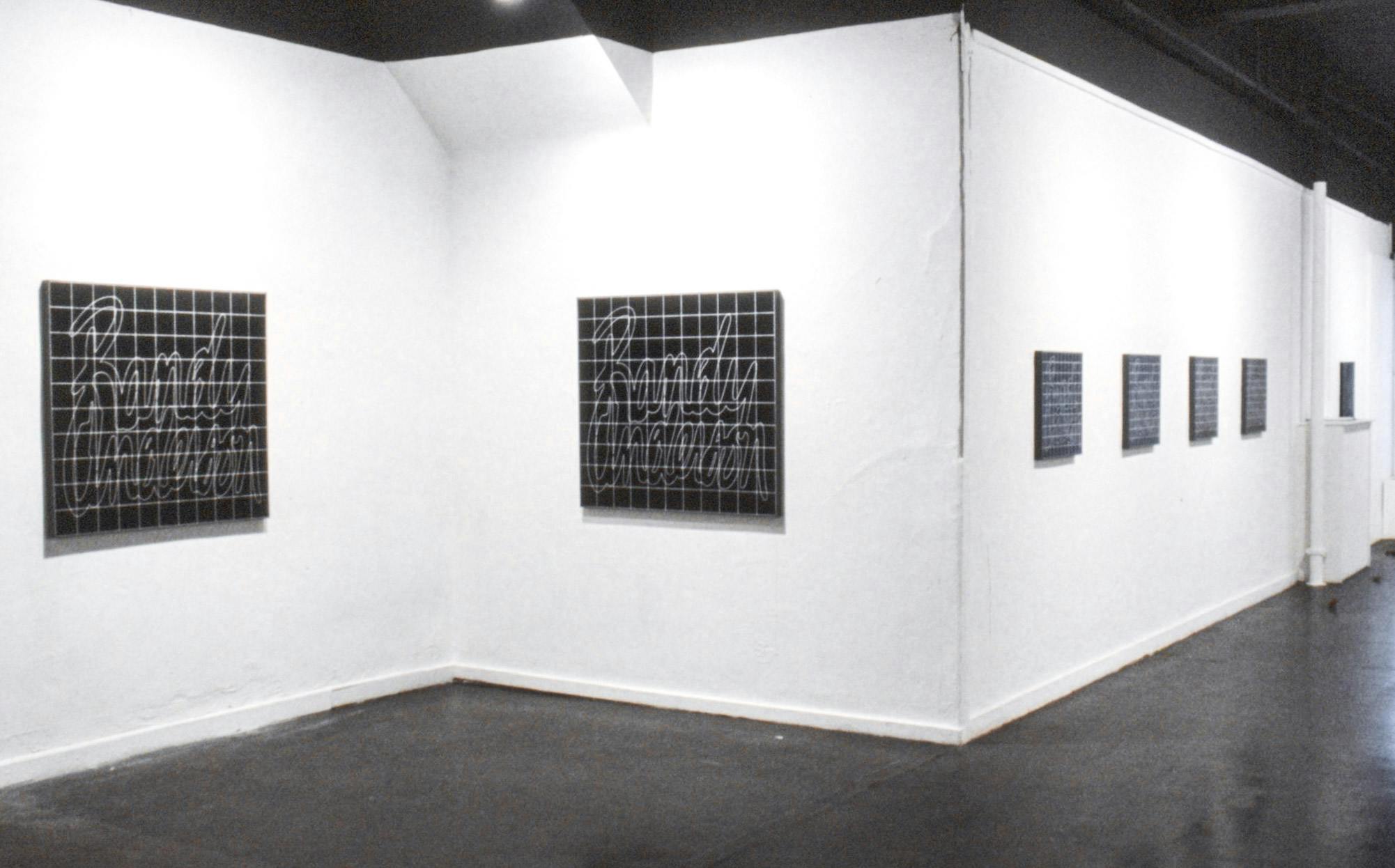Rows of nearly identical paintings across the walls of a gallery. They are black with white outlined text reading "Randy Anderson" and a white grid on top.