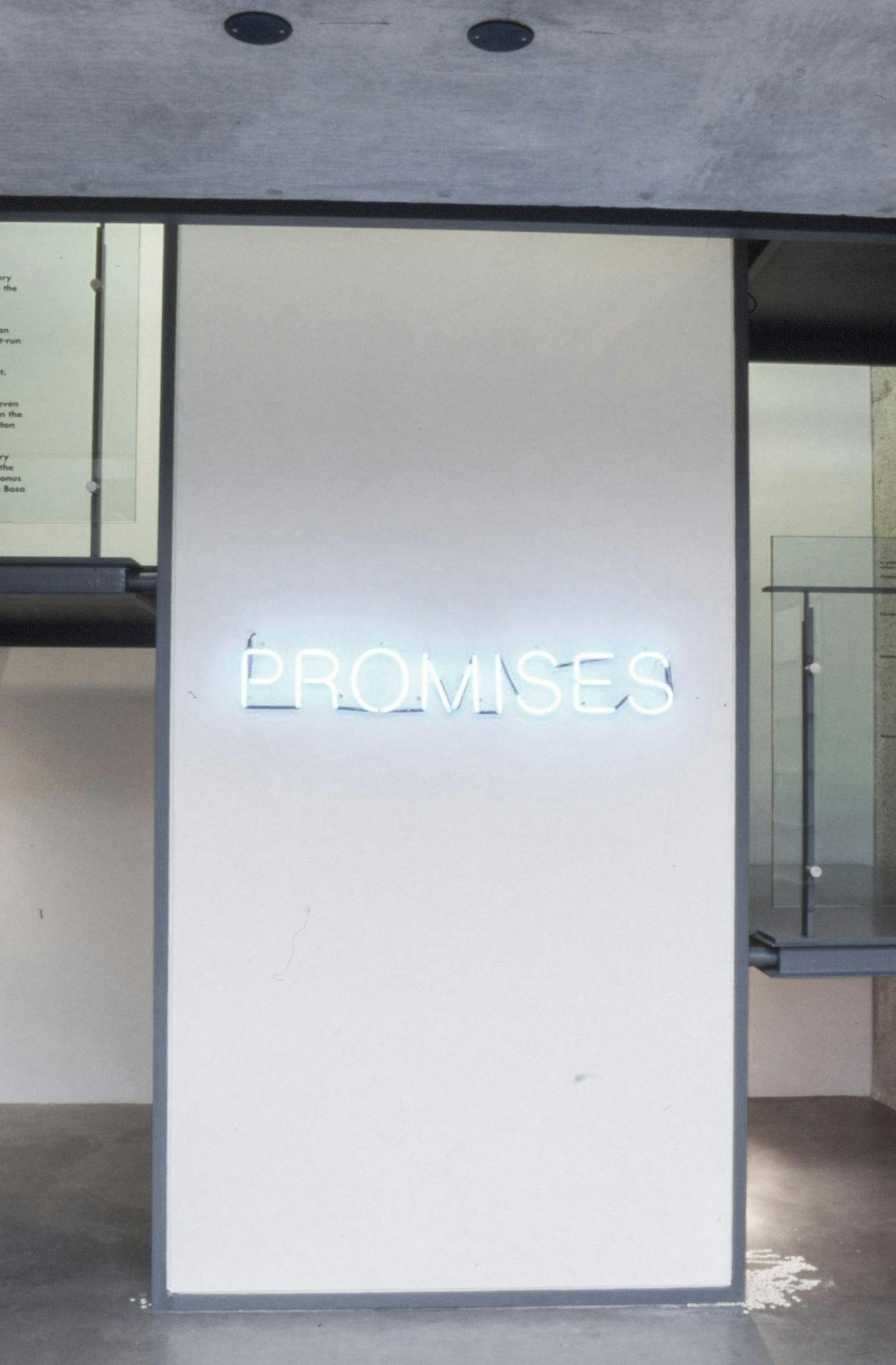 A blue-white coloured neon sign is installed on the wall in a gallery space. The sign shows the exhibition title, PROMISES. 