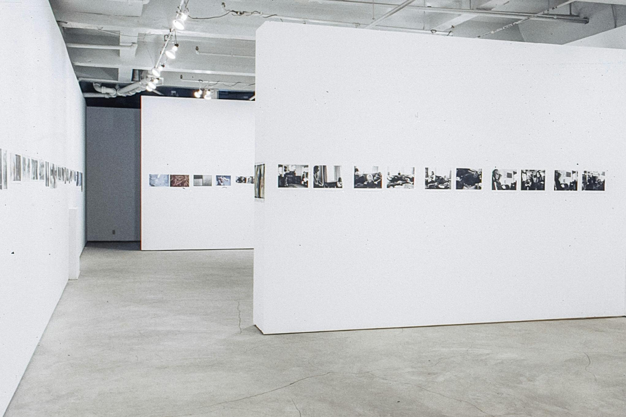 A large gallery space with a white wall in the centre. Across all visible walls, there are a variety of colour and black and white photographs of slightly different sizes.