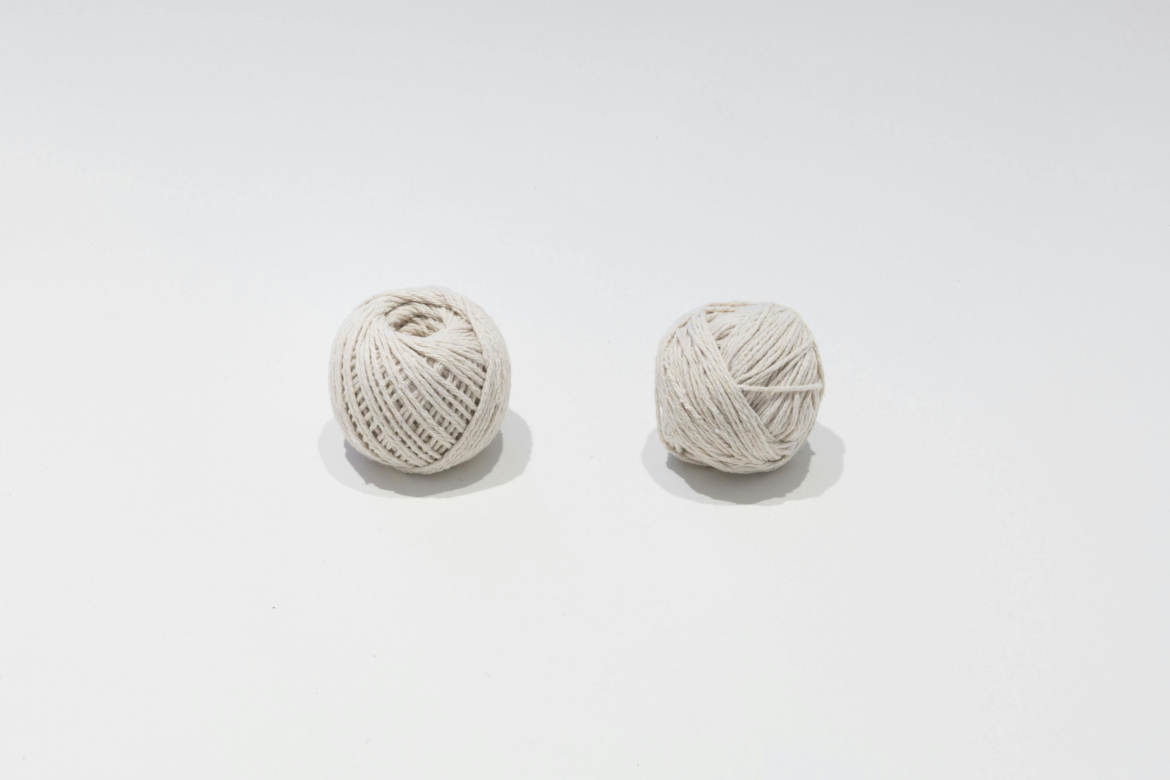 Two balls of white string placed on a white flat surface. The left ball is slightly more neatly rolled than the one on the right. 