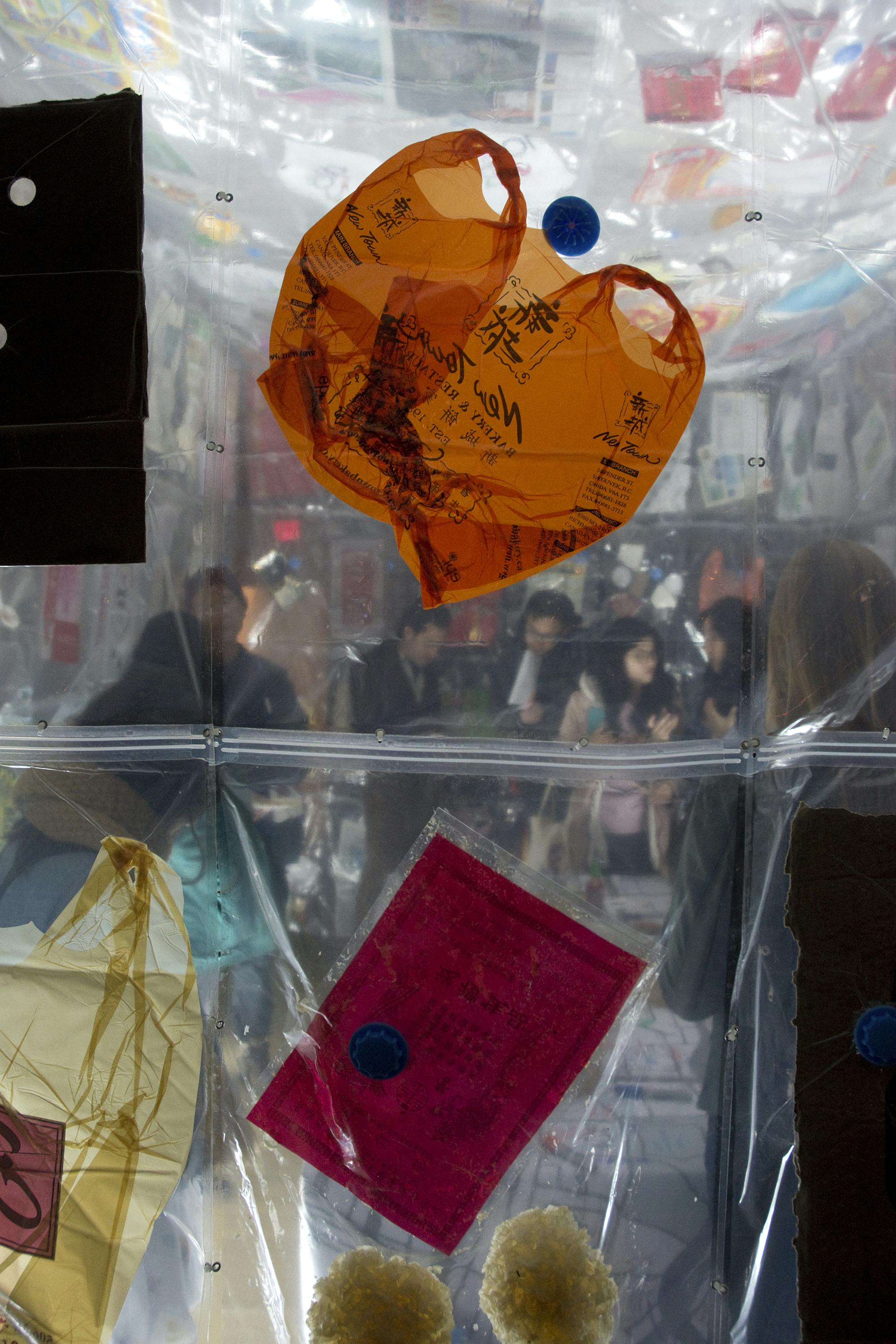 Various items including plastic shopping bags are vacuumed sealed in clear bags. People are visible through the clear bags.