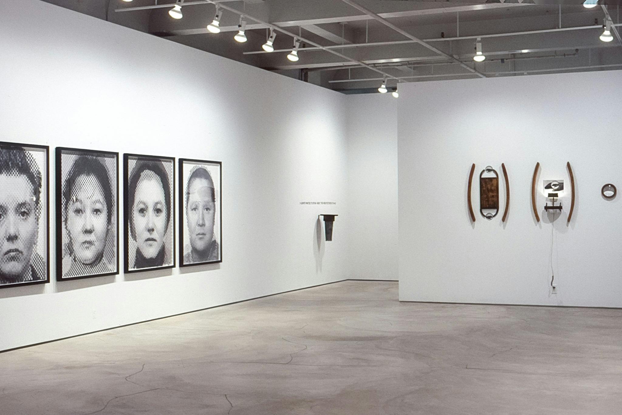 An installation view of the gallery. Various artworks including black and white large-scale photographs of people’s faces and found objects are mounted on the walls.