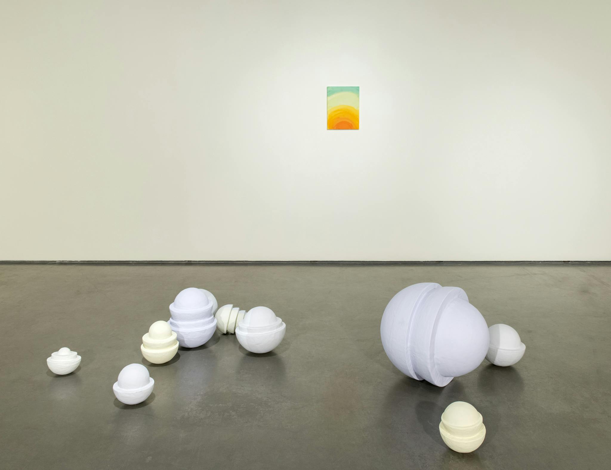 Nine ceramic sculptures installed on a galley floor. Each sculpture resembles stacked ceramic bowls with a sphere in the middle, painted in either a pale yellow, white, or blue.