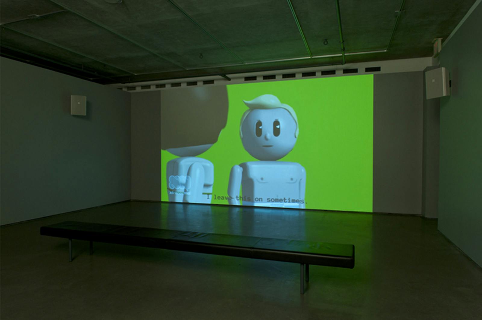 A single-channel video is projected on a wall in a darkened gallery space. The scene depicts a toy-like, animated man speaking “I leave this on sometimes” to another character, a toy-like woman.