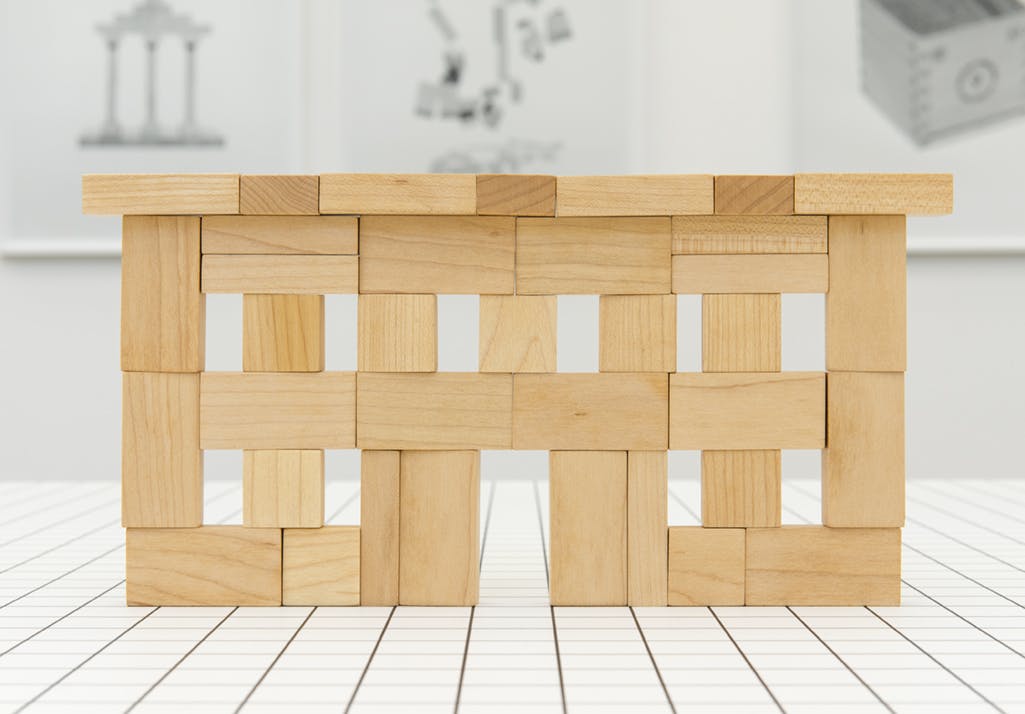 Detail image of stacked wooden blocks on a white table resembling a simple facade structure