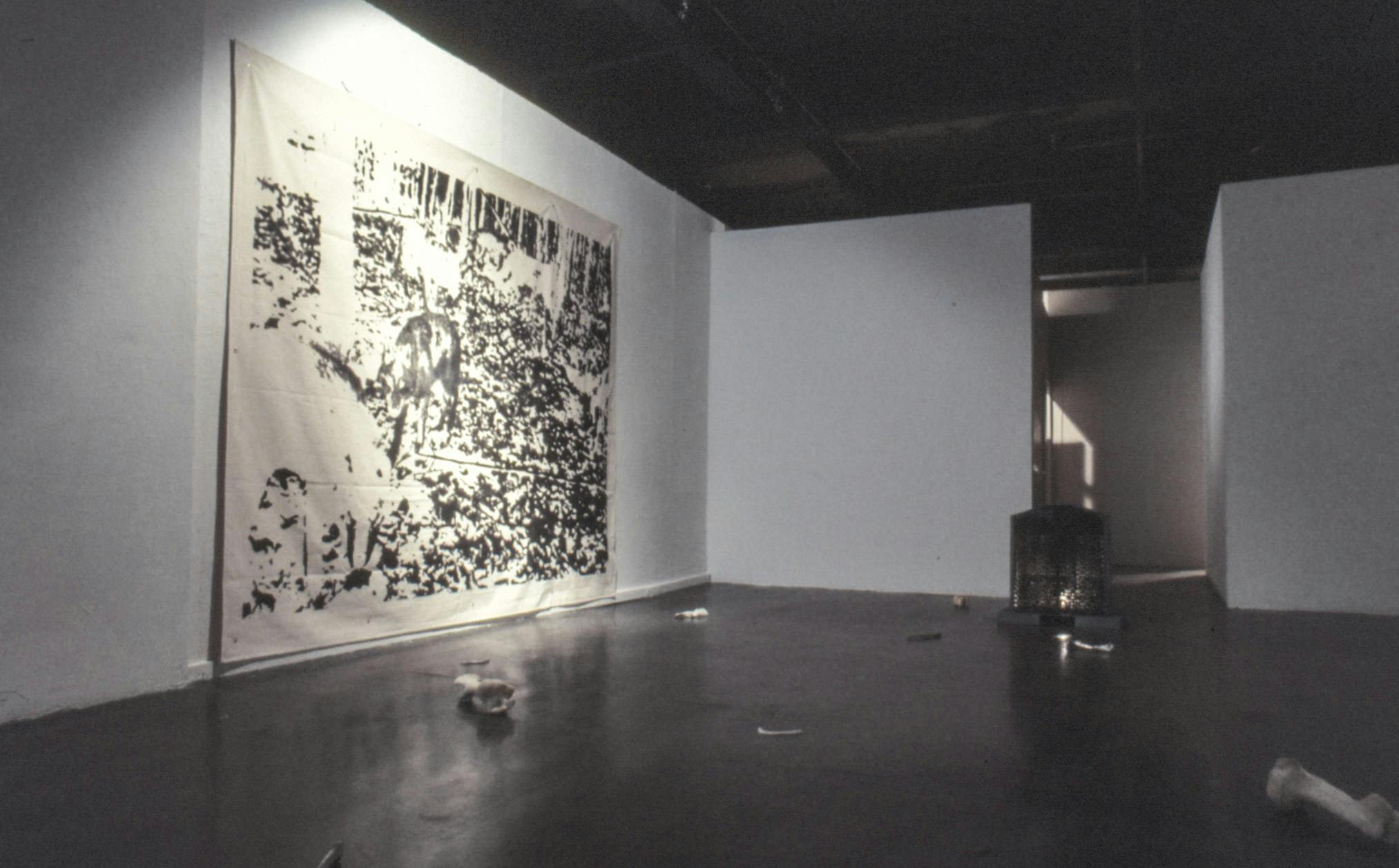 On the floor of a dark room in a gallery, there are human, animal and cast steel bones. On one wall, a very large piece of canvas shows a negative screen print of wolves in a forest.