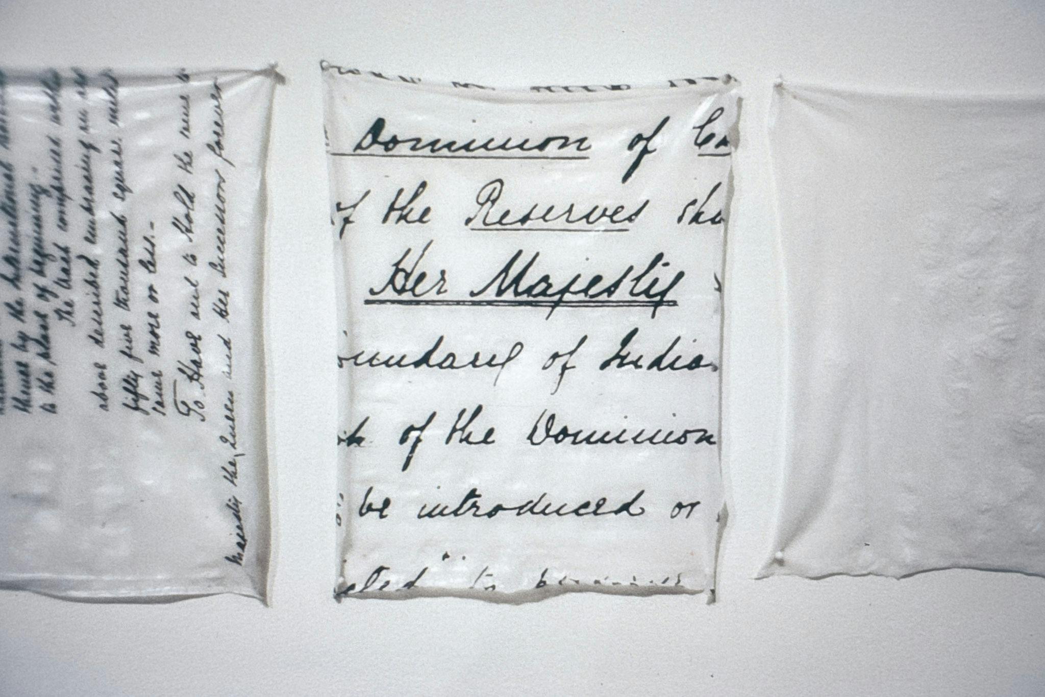A closeup of 3 artworks on a white wall. They are made of thin glossy material, stretched out and pinned. 2 of the works include enlarged text from hand-written documents about the queen of England.