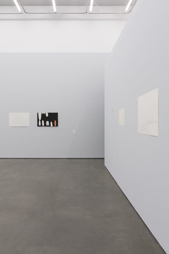 Drawings and paintings by Jürgen Partenheimer installed on two gallery walls. One is a black, abstract watercolour painting with several white and orange oval shapes.