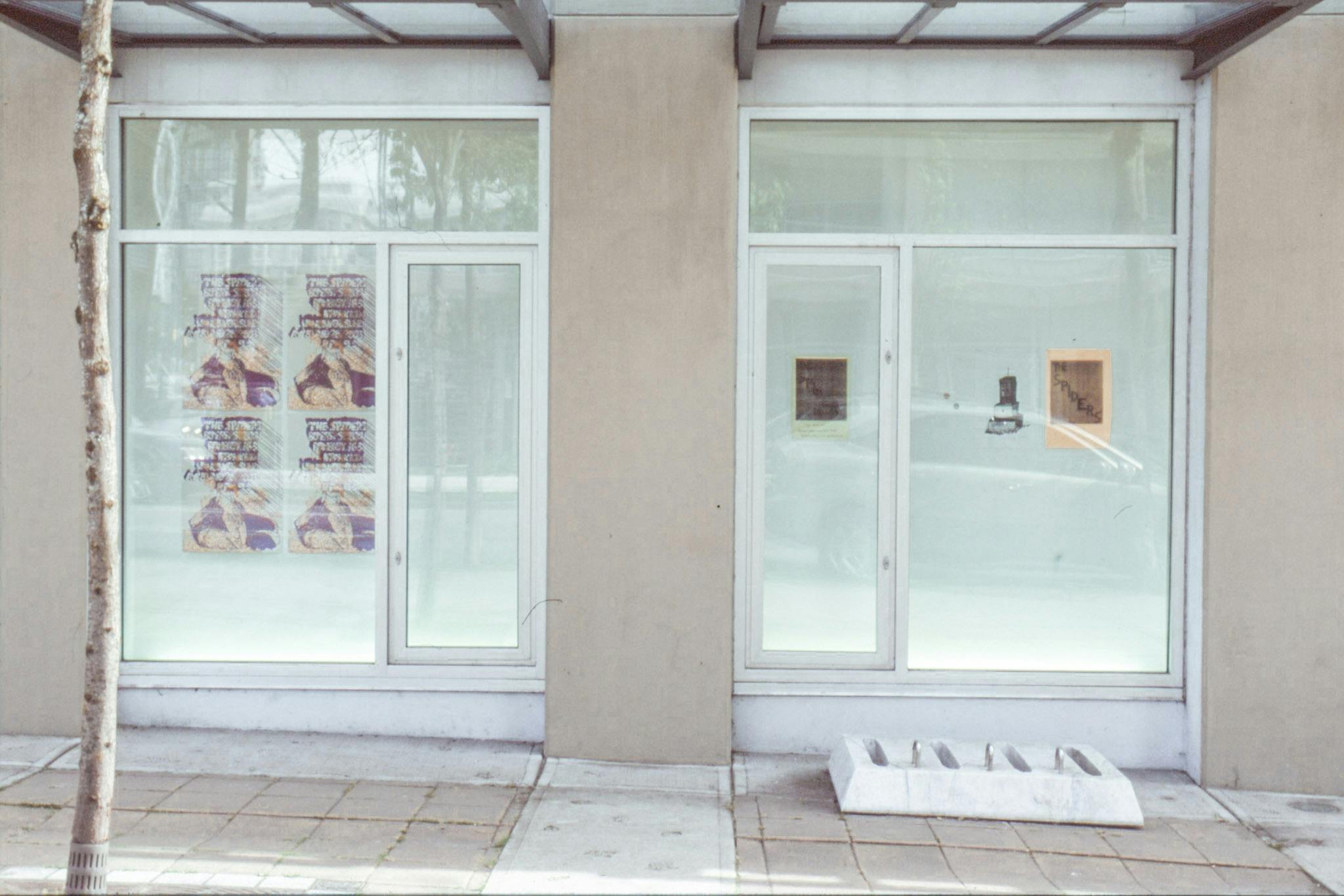 An install image of two-dimensional works in CAG’s window spaces facing Nelson Street. Exhibited works look like a collection of various ephemera such as posters and pamphlets.