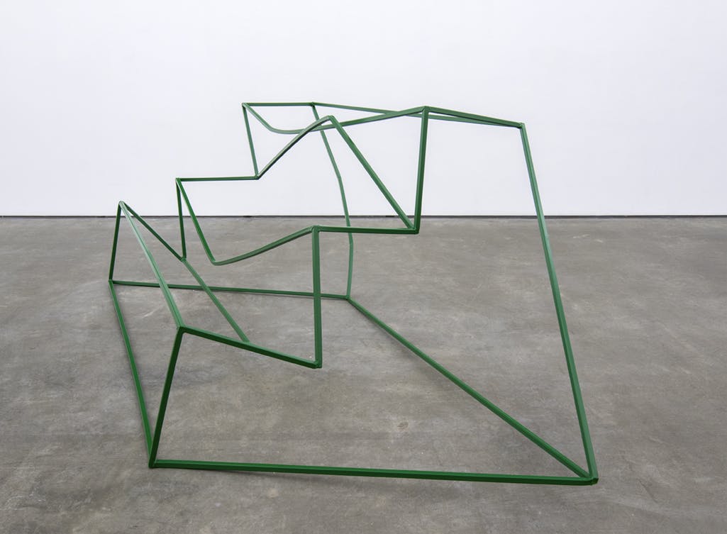 A free-standing, steel sculpture by Monika Sosnowska installed in a gallery. The form resembles a steel frame for a three-step stair. The frame is bent and its surface painted green.