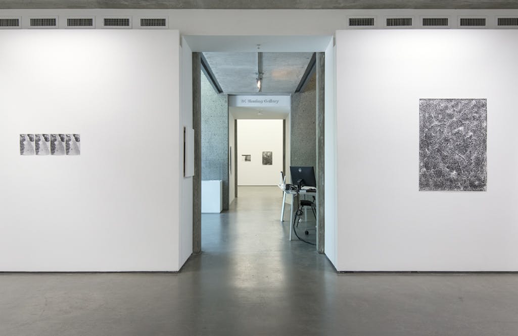 Two black and white photographs hang on walls in a gallery separated by an entryway. Two more black and white photographs are visible through the entryway, across a lobby, into another gallery.  