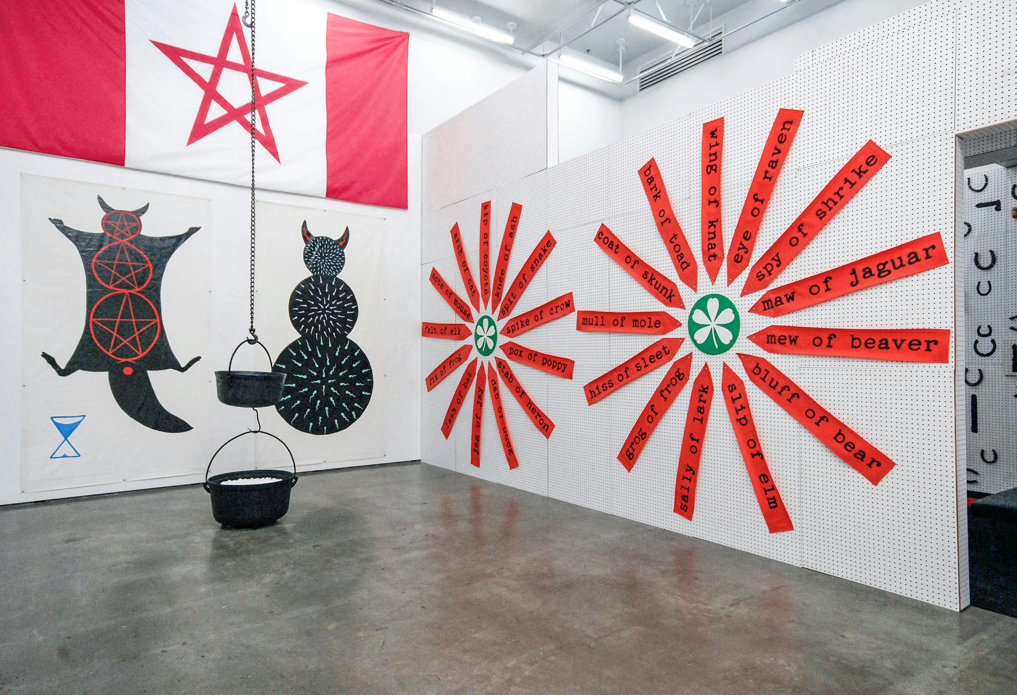 Flags, large posters, and handwritten signs cover the gallery walls. Red, black, and white are prominently used in those images. Two black cooking pots are hanging from the ceiling.