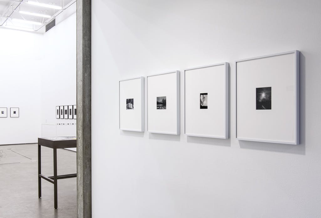 Four small black and white photographs appear in a corridor leading to a larger gallery, where many works are installed. 
