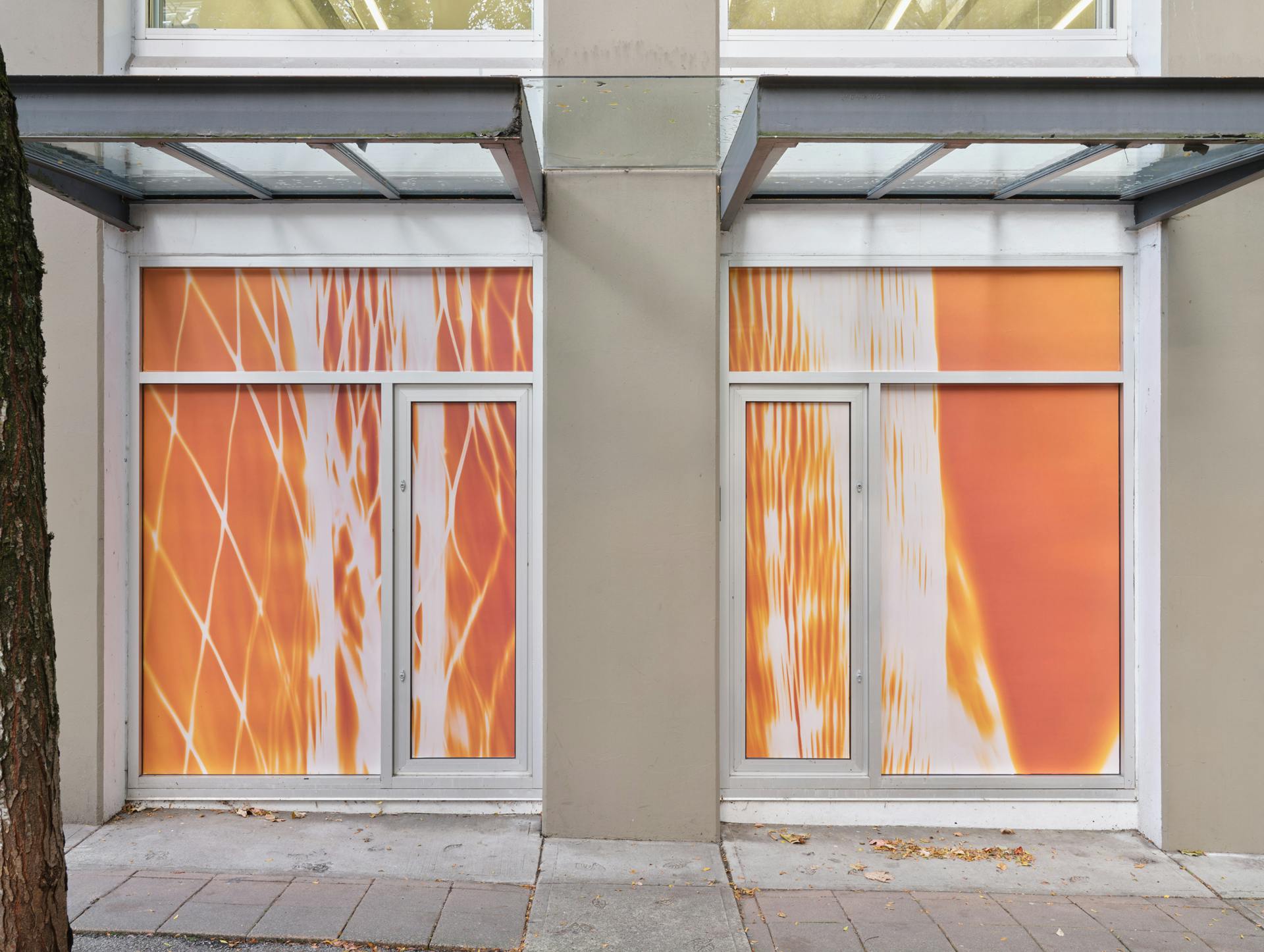"A pair of windows featuring a pair of photograms depicting nylon mesh produce bags against neon orange backgrounds."