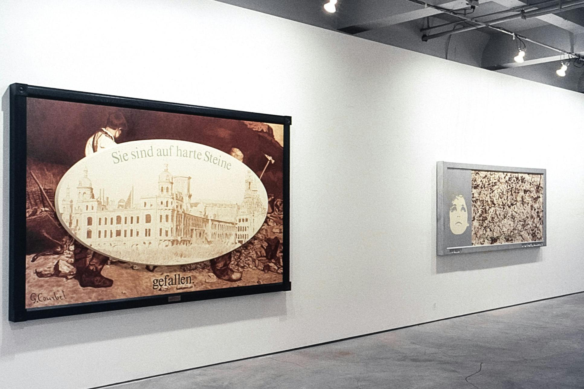2 large framed paintings in a gallery. One is a sepia-toned painting showing two young people splitting rocks with pickaxes. In the foreground there is German text and a long building in a white oval.