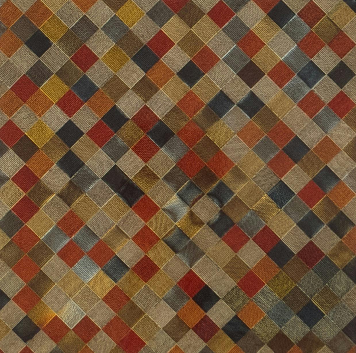 Detail of an artwork. The work is made with various textiles woven together, or placed next to each other, to create a repetition of small squares. The colours of textiles used in this work are gold, silver, blue and orange. 