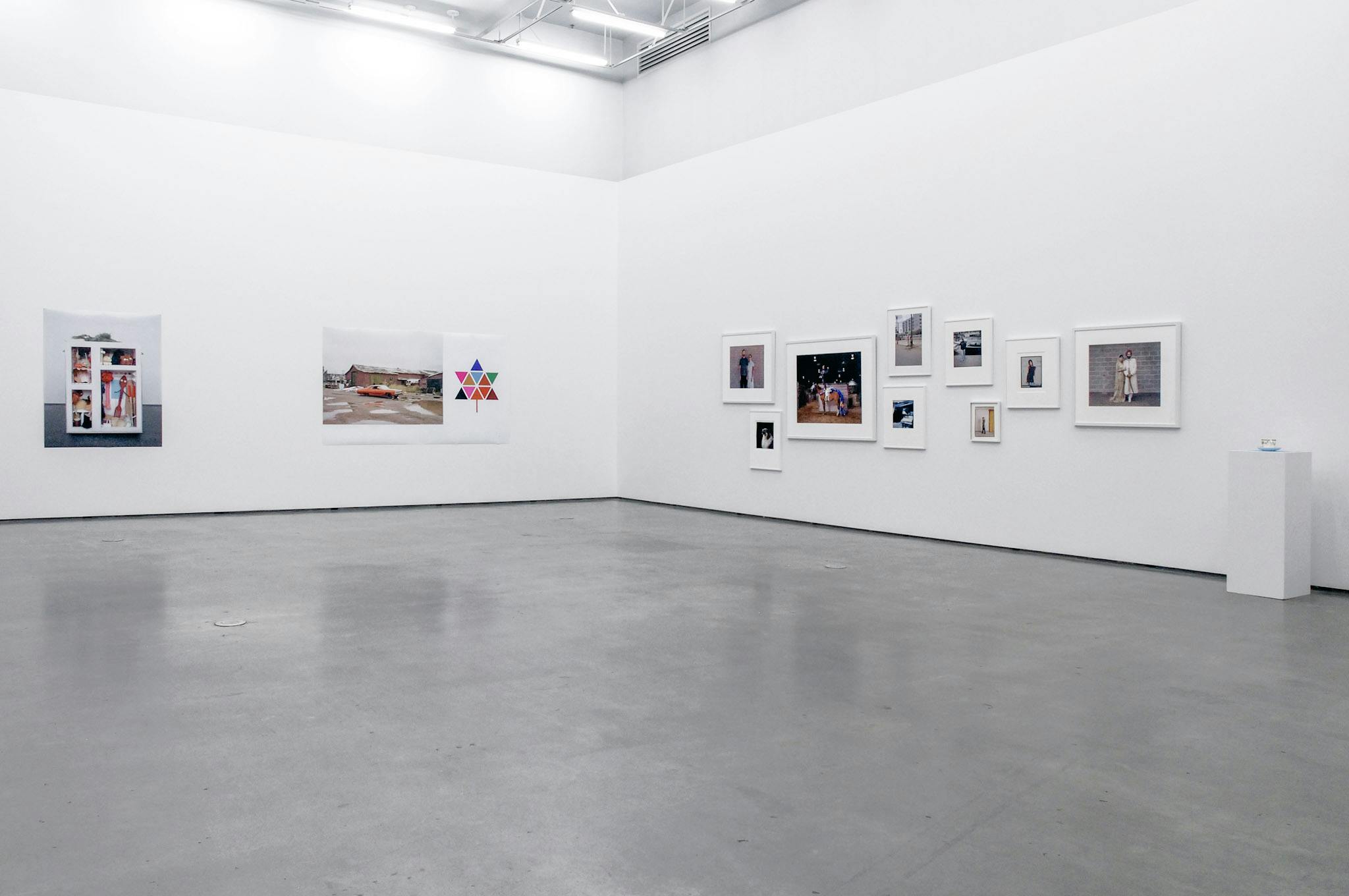 This is an installation shot of Chris Gergley’s art photography exhibition. Various sized coloured photographs, some framed and some unframed, are mounted on the gallery walls. 