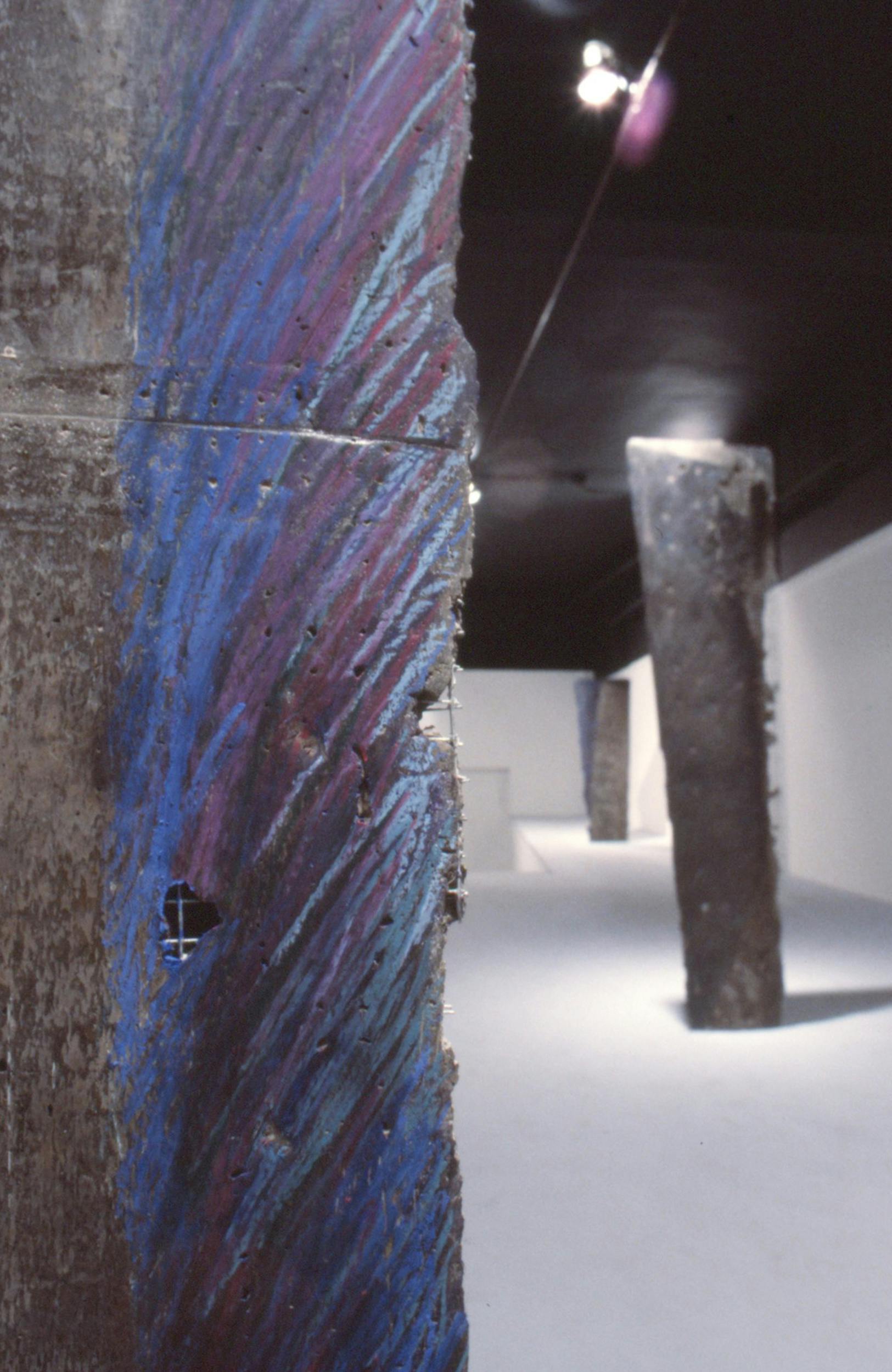 A close up view of a sculpture made of cast metal. The edge of the sculpture is coloured gestural strokes of blue and purple pastel. 