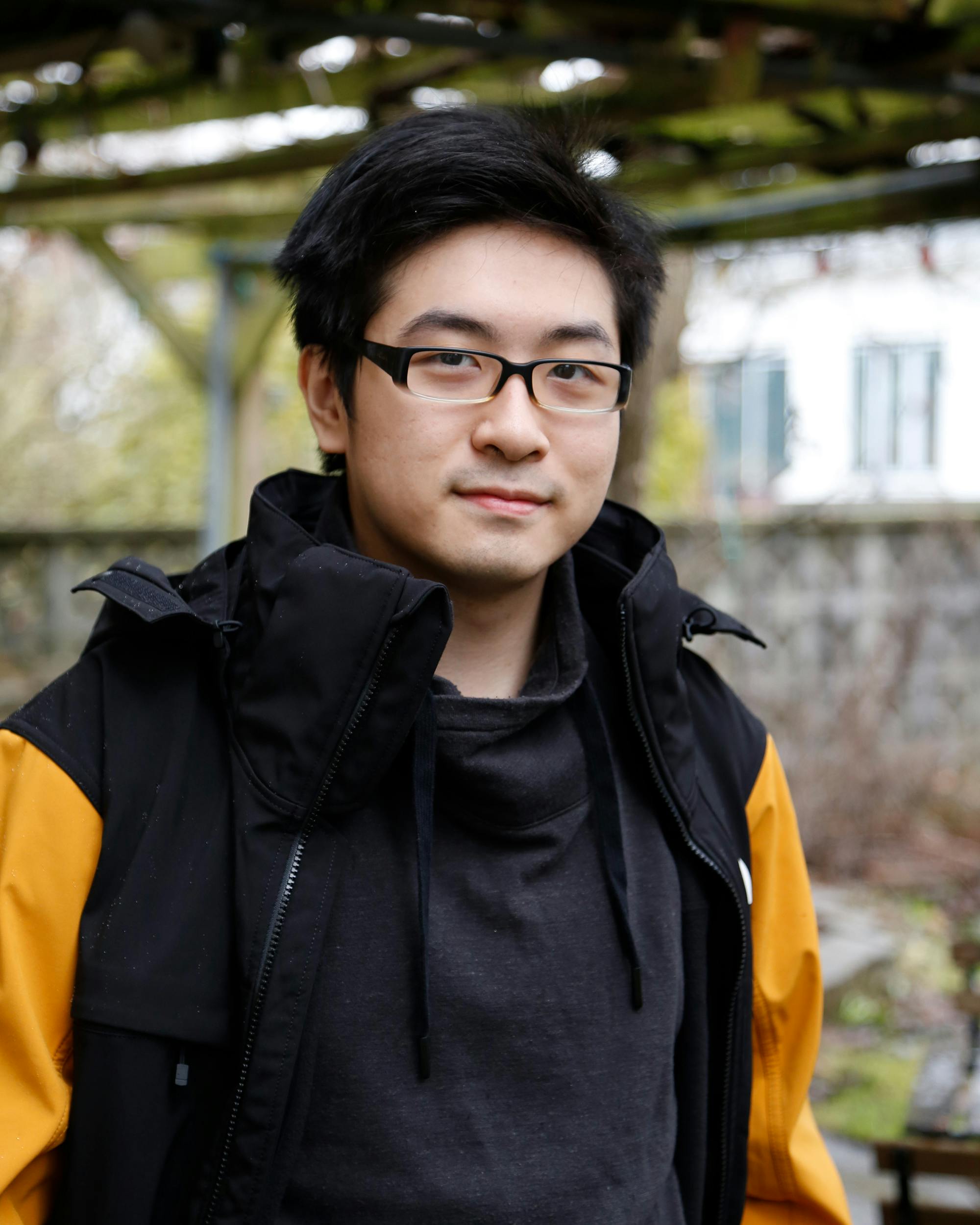 A photo of Silas Ng. He is wearing glasses and a black raincoat with yellow sleeves.