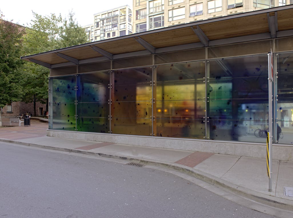 A photographic mural in vinyl is installed on the windows of Yaletown-Roundhouse Station. Black dots scatter across a semi-translucent background of softly focussed yellows, blues and greens. 