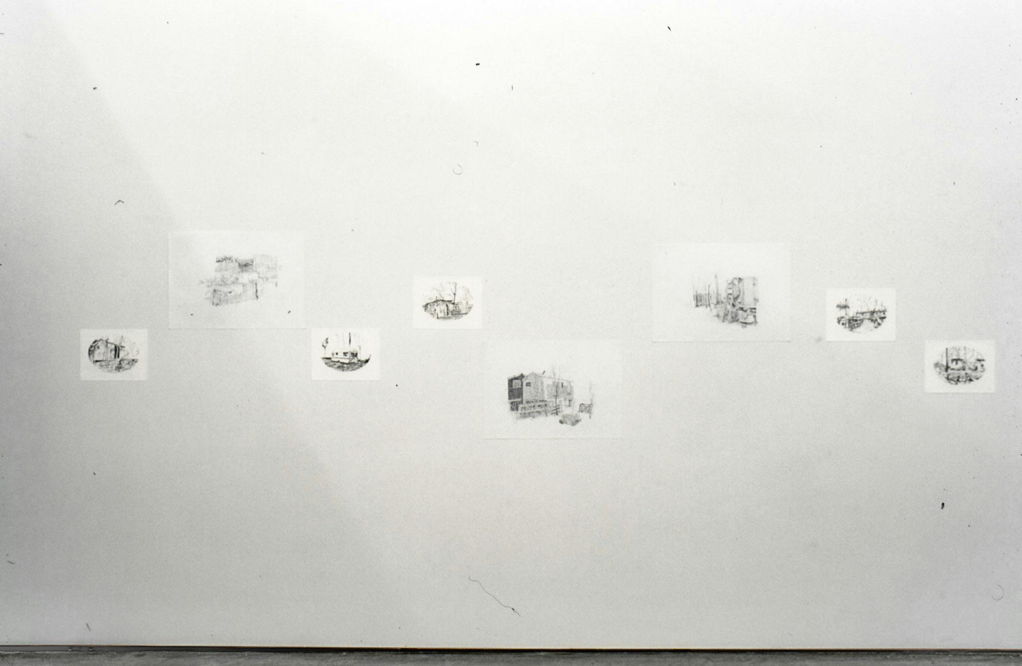 Installation image of drawings by Alex Morrison. 7 black and white drawings of buildings on various sized paper are mounted on a wall. 