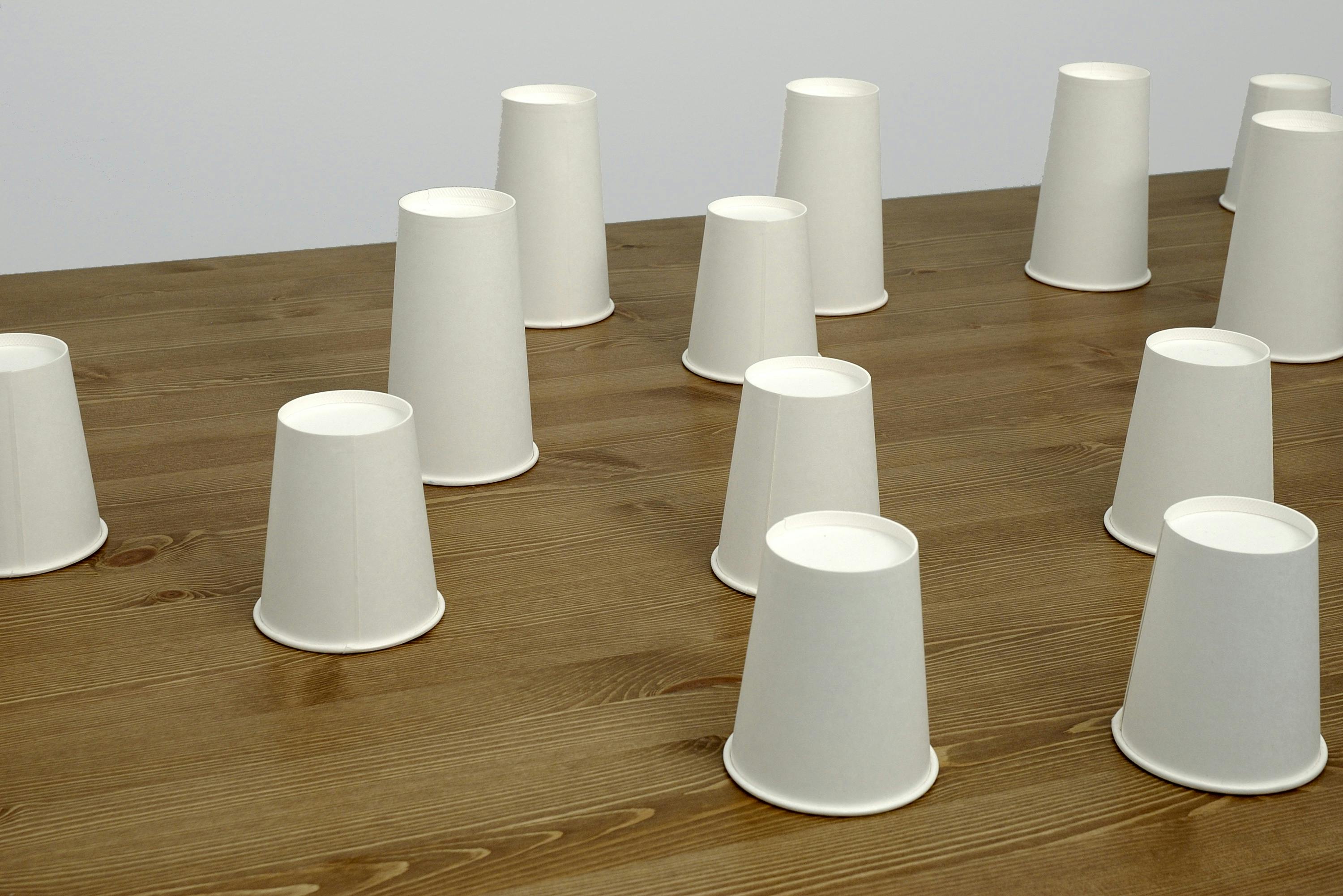 Rows of upside down white paper cups are placed on a wooden table.