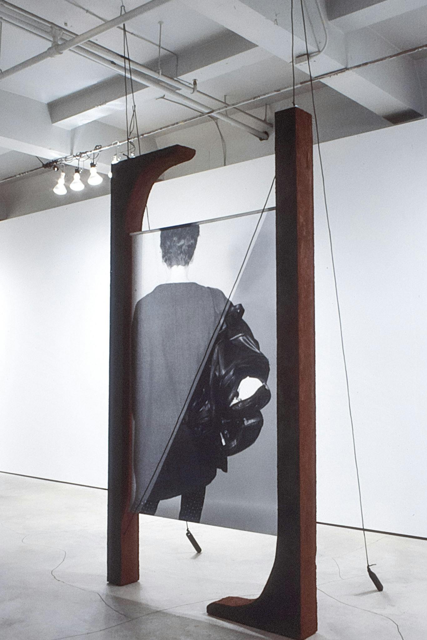 A large photo stretched between two wood beams. The beams have a slightly curved foot to them, resembling a serif on the letter "N." The structure has cables that hang from the ceiling attached to it.