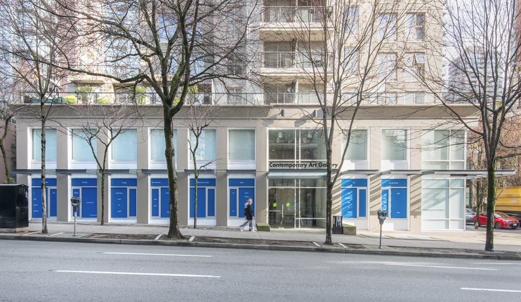 Exterior image of CAG’s first floor facade installed with text-based work in vinyl by John Wood and Paul Harrison. Text is white on a blue background.