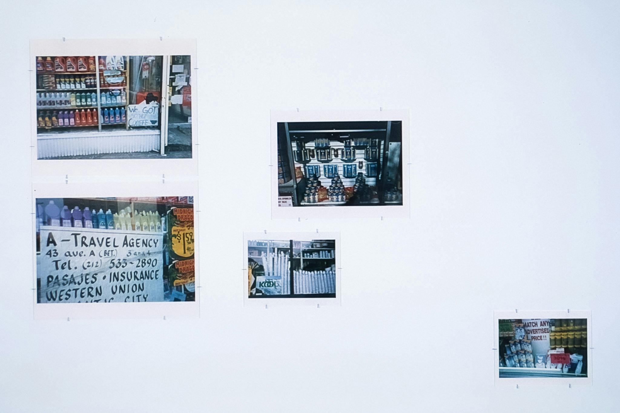 Five coloured photographs of various sizes are displayed on white a wall. All photos depict storefronts. Some have handwritten signs that read, “We Got Coffee” and “Match Any Lower Advertised Price!!”