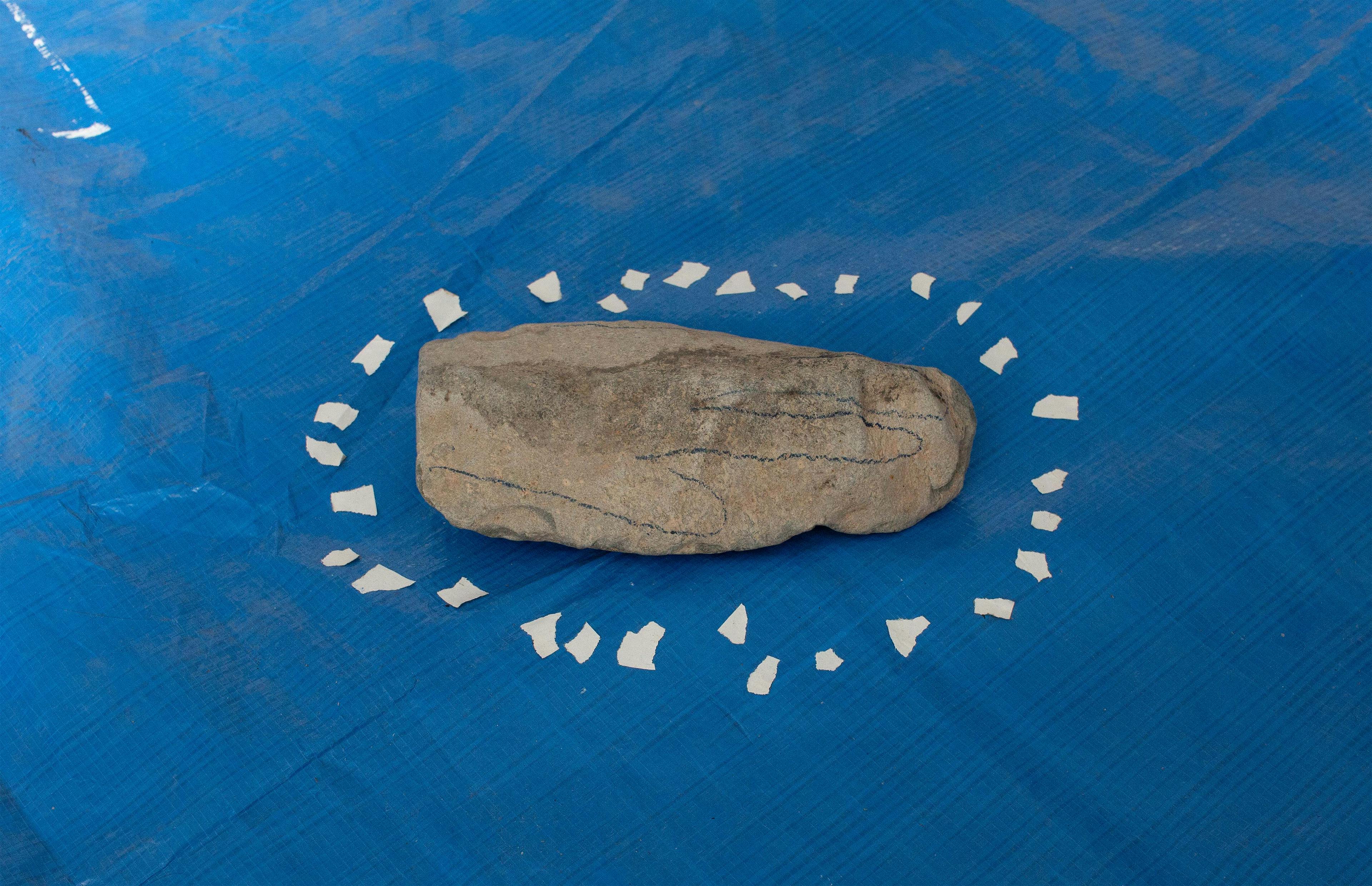 A stone with the outline of a handprint is displayed on a blue tarped surface.