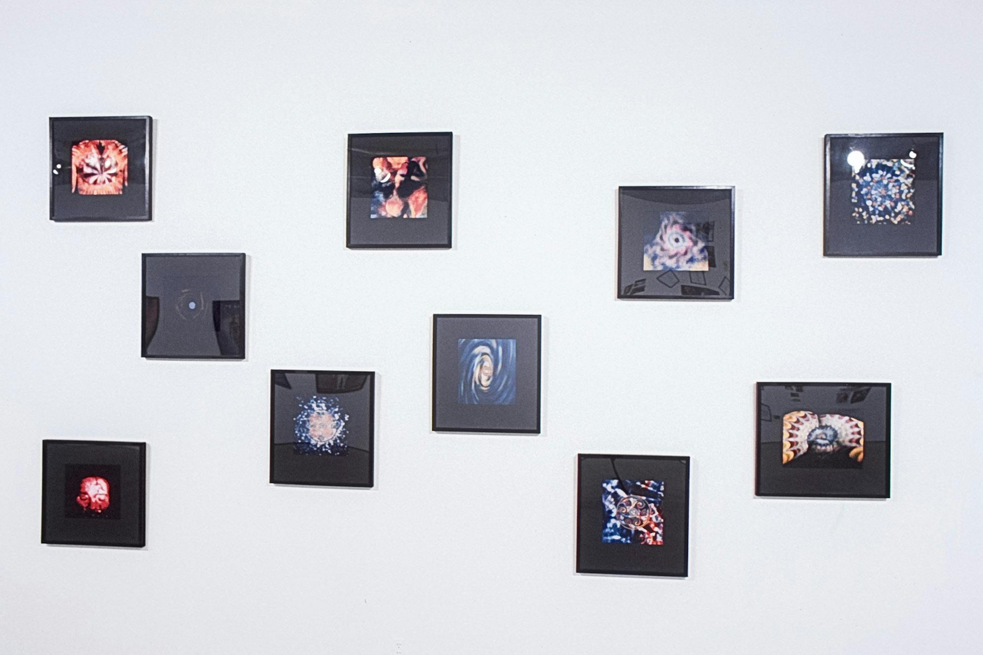 Several images in black frames, mounted on a white wall. The images are colourful and detailed, resembling views from a kaleidoscope. The photo is at a slight angle and shows the frames diagonally. 