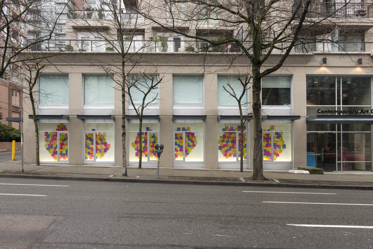 Dozens of coloured sticky notes mounted in windows across CAG’s exterior facade. The notes partially overlap with each other to form three different groups in continent-like shapes.