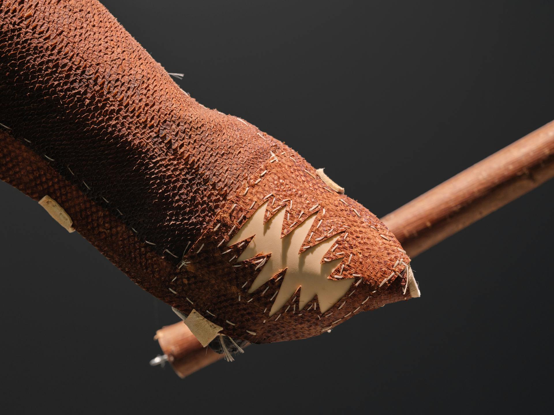 the bottom half of a fishskin leather arm cover, arranged to look as if it's holding a wooden shaft. the hand of the arm cover bears a zig-zag patterned shape. fish scales are visible in the texture of arm cover throughout.
