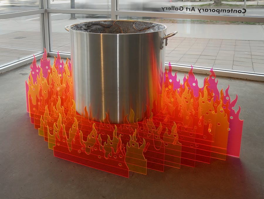 A large cooking pot sits on top of rows of plastic fire. Each row of fire varies in shades of red and yellow. Each row gets longer the further back it goes. 