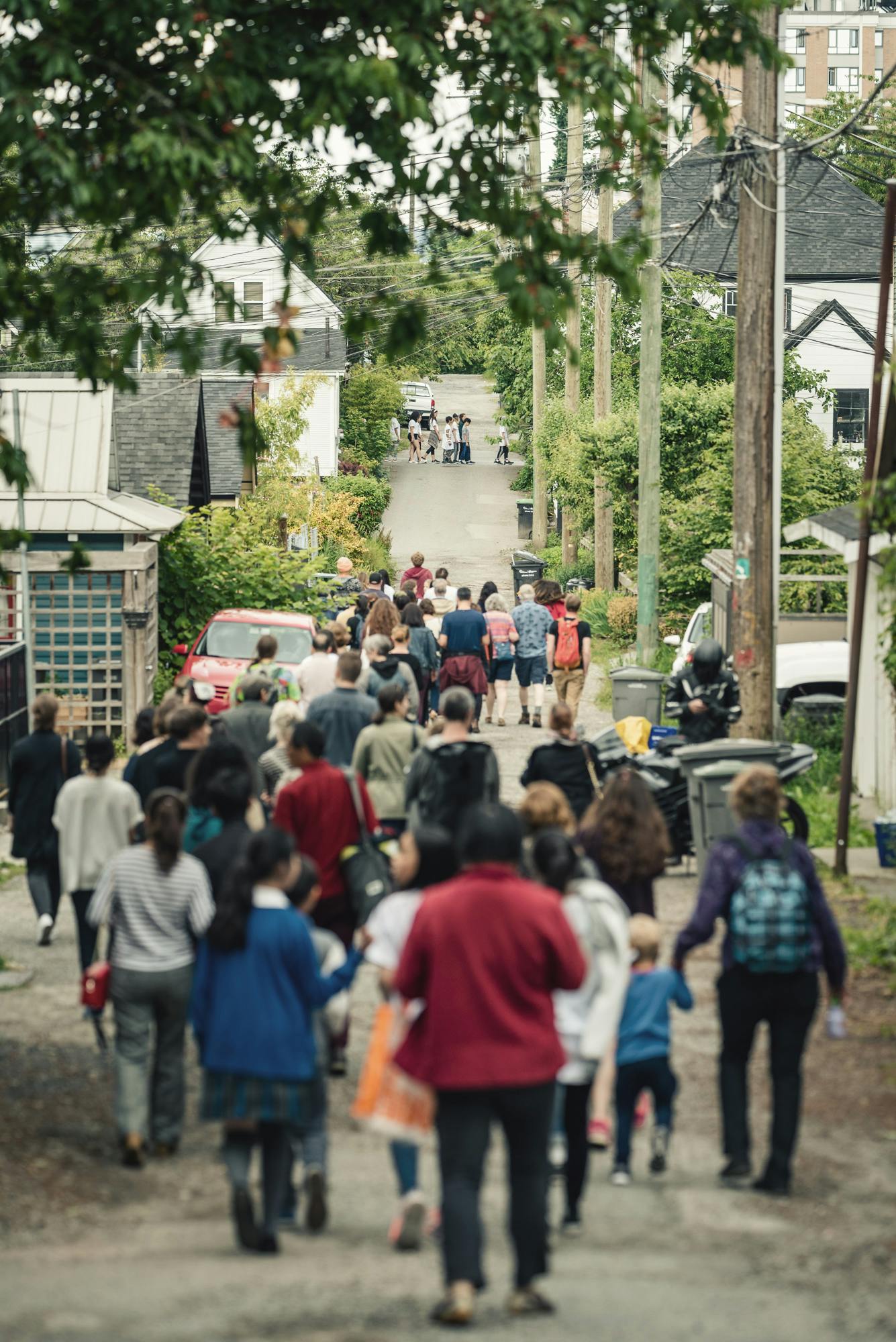A photograph of children and adults walking down a narrow alley between houses. 