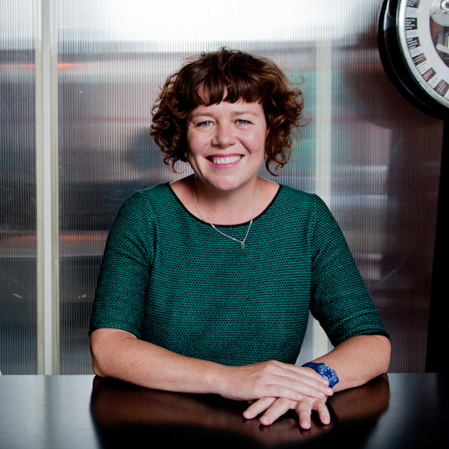 A portrait photograph of Sally Tallant smiling. Tallant is wearing a green shirt and a silver necklace. 