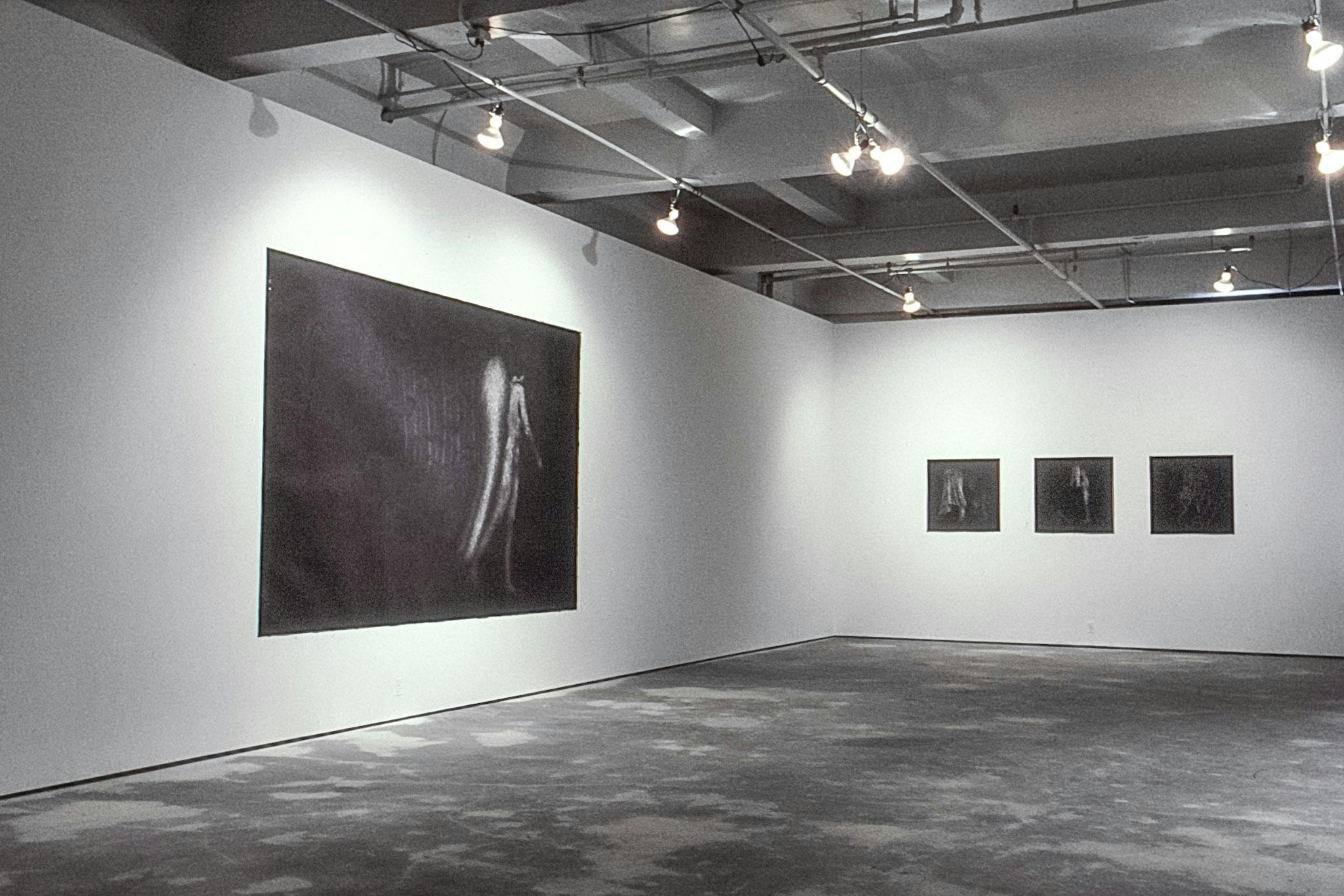 On one wall of a gallery, there is a large charcoal drawing of a nude angel walking. On the other wall, there are three small square drawings showing fabric and bodies. All drawings are very dark.
