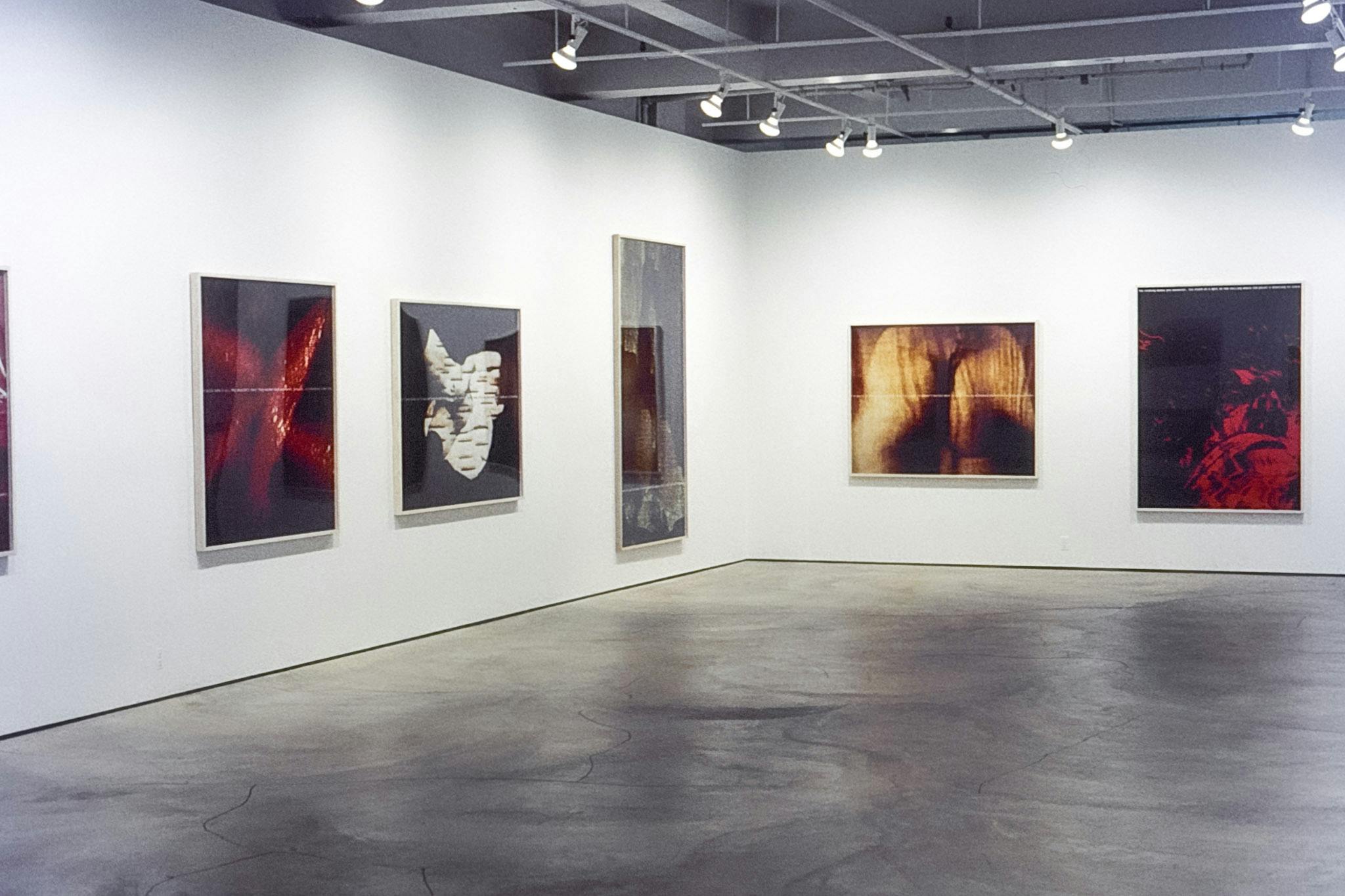 Five artworks mounted on two gallery walls. Two of the pieces have red organic shapes on black background. The second piece from the right captures a figure that resembles a bent naked human torso.