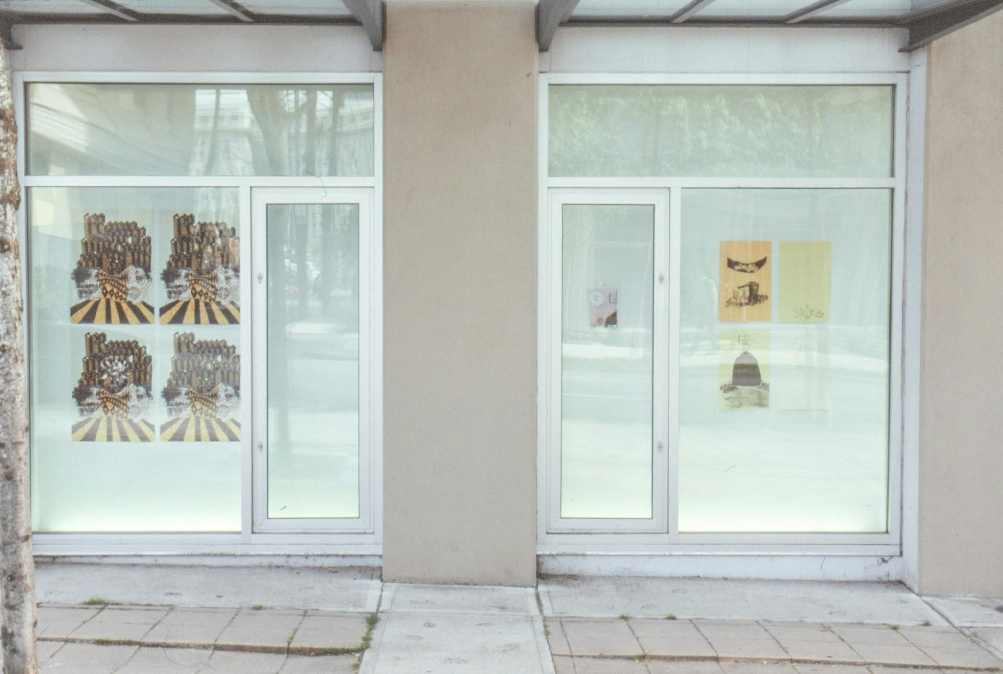 An install image of two-dimensional works in CAG’s window spaces facing Nelson Street. Exhibited works look like a collection of various ephemera such as posters and pamphlets.