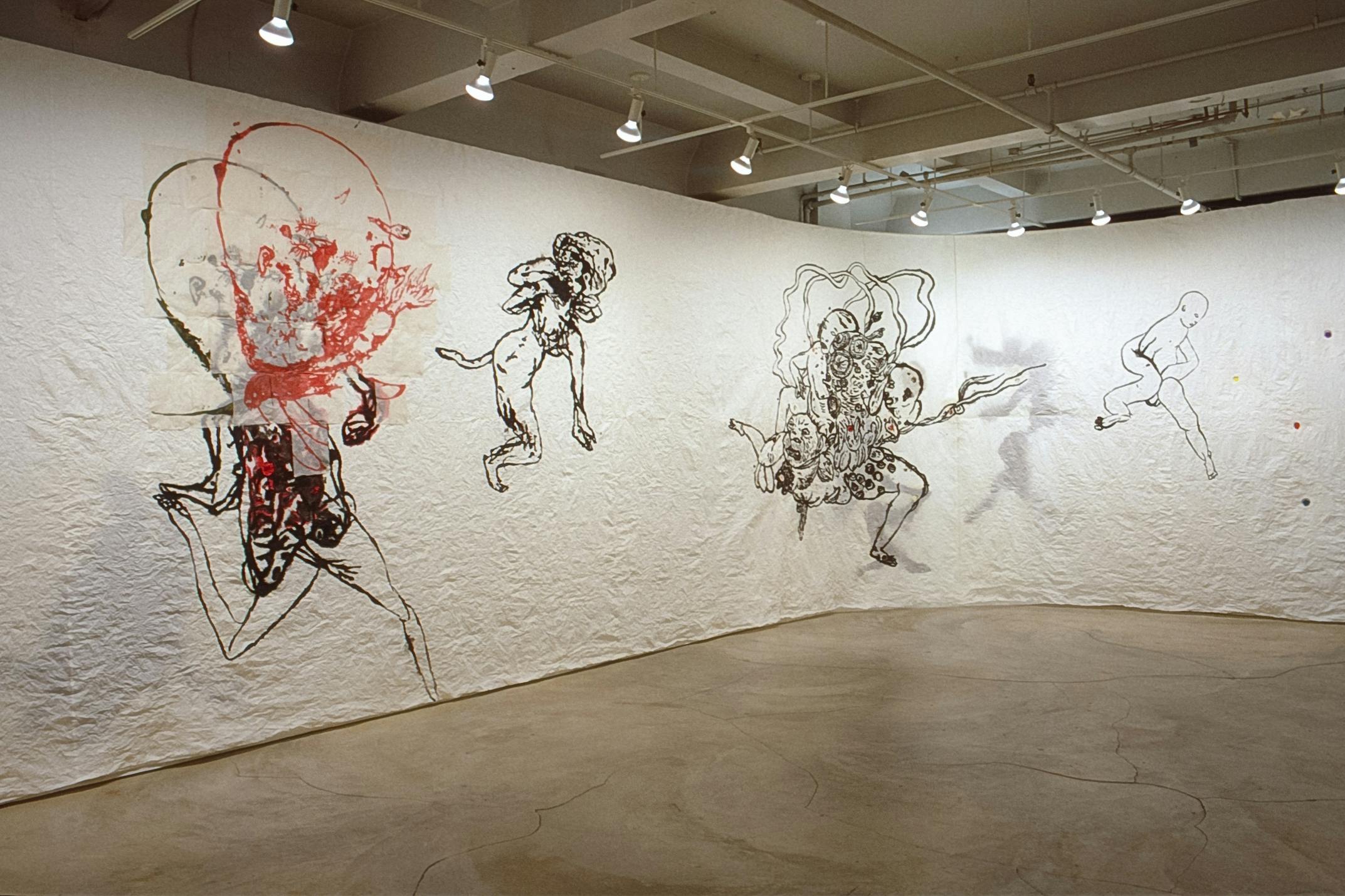 Gallery walls are covered by a wide white scroll of paper, on which Ed Pien’s drawings are made. One of the drawn figures has an inflamed huge head in red over the naked body outlined in black. 