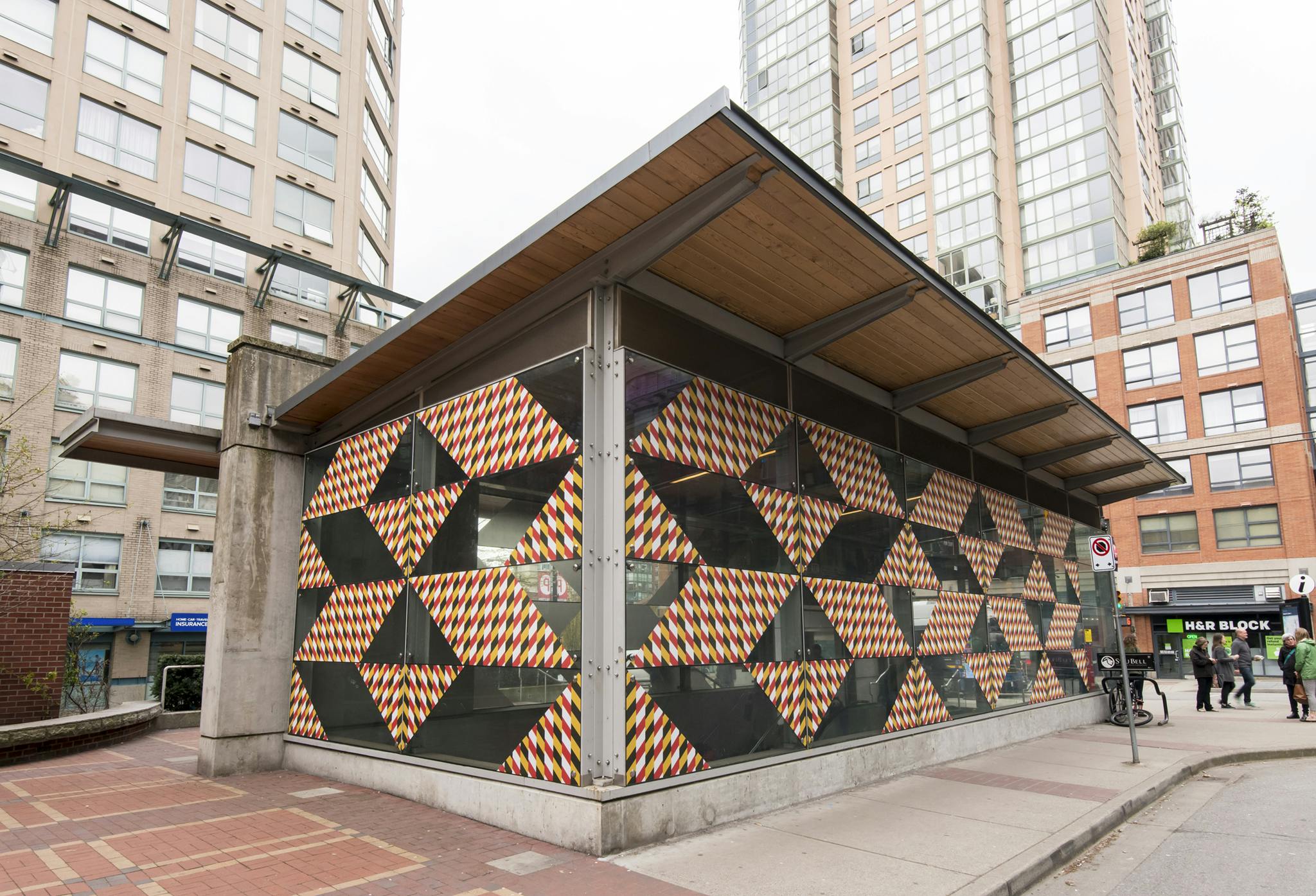 Exterior image of the Yaletown-Roundhouse station façade covered in a pattern of vinyl rhombus and triangle shapes. Each shape contains patterns of alternating red, white, black and yellow rhombuses. 