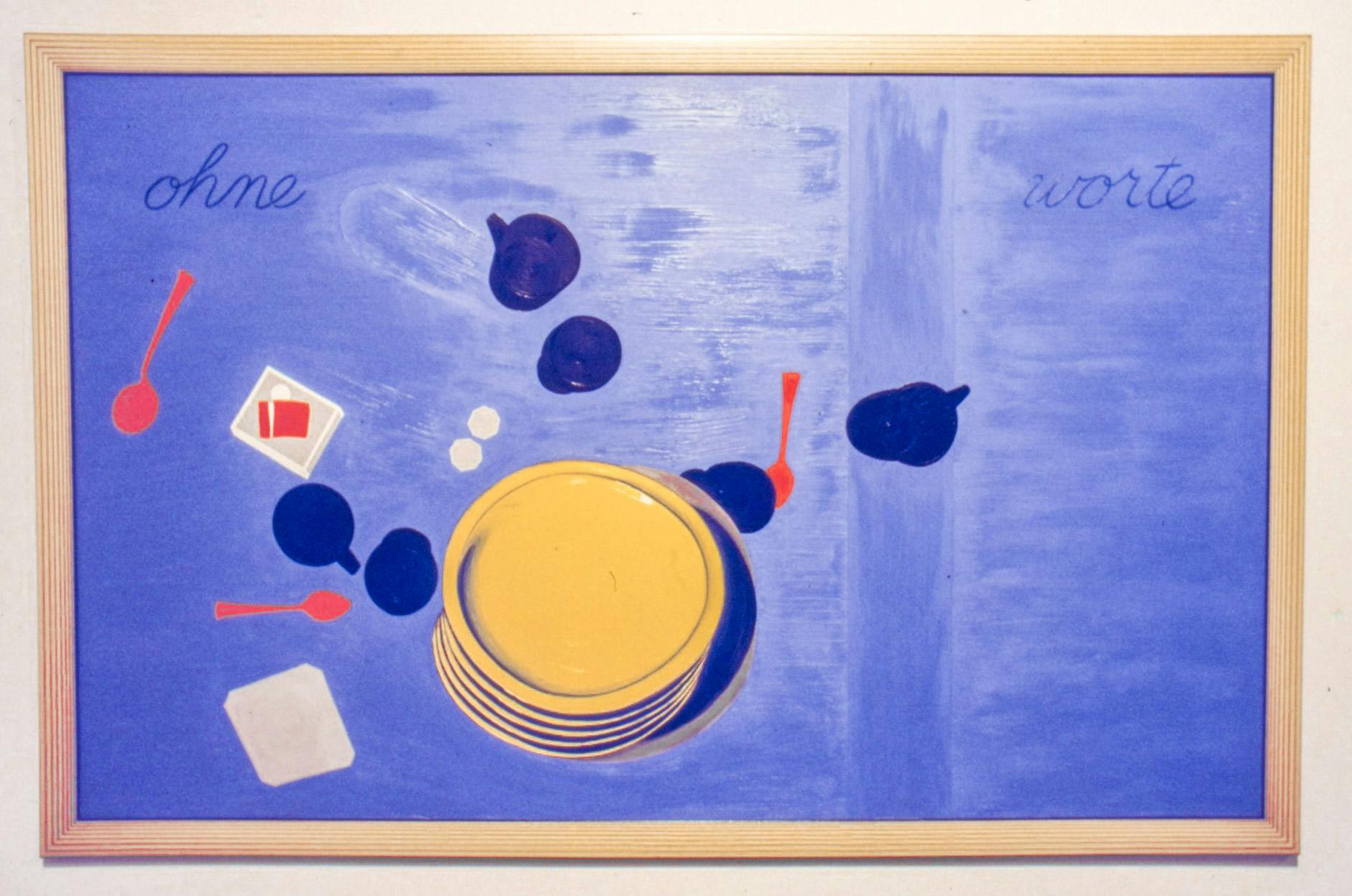 A closeup of a painting in a wood frame. It shows yellow plates, blue cups, and red spoons on a purple background.  Text on the top corners reads "ohne worte" meaning "without words" in German. 