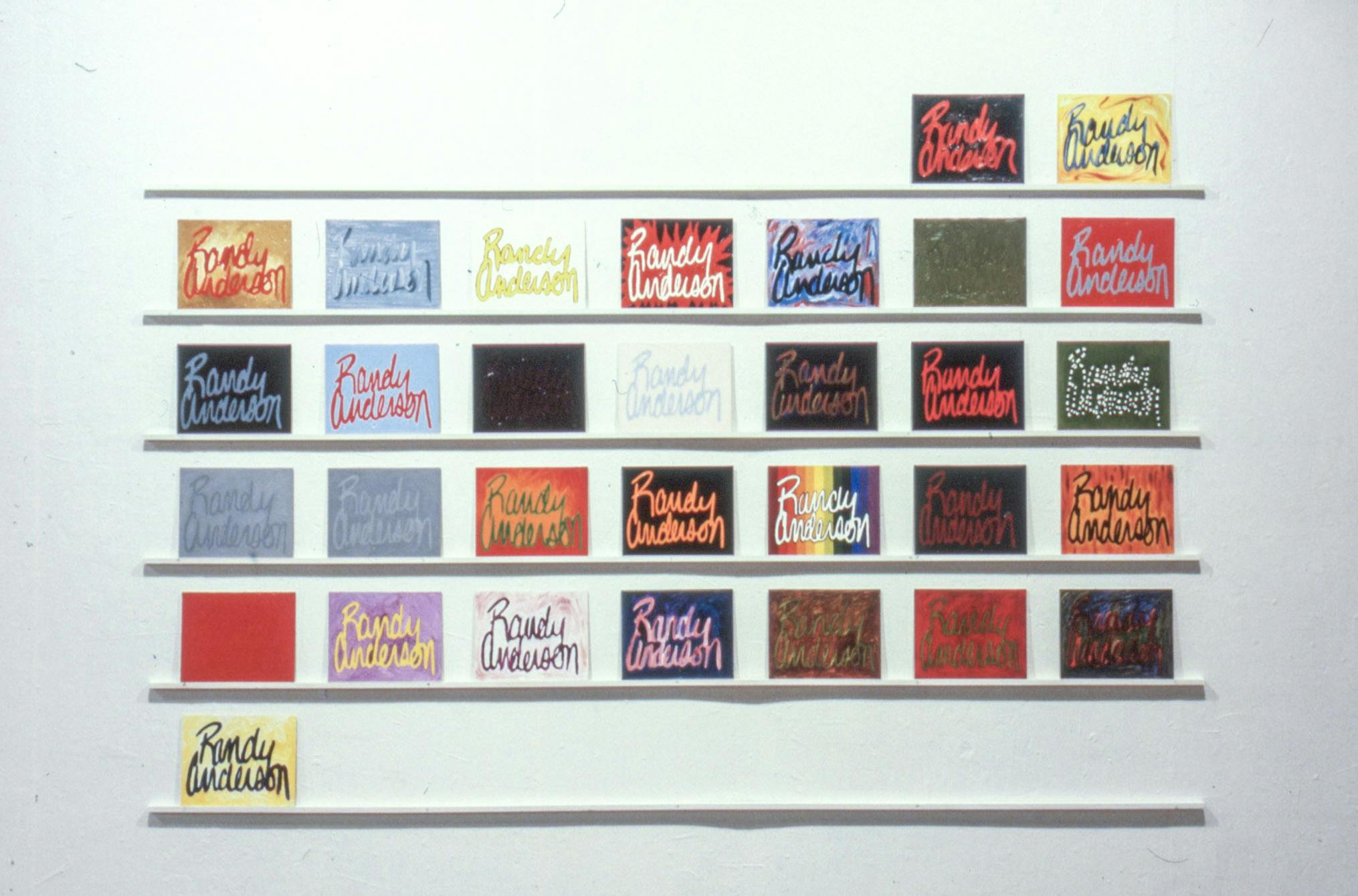 A close-up of 31 small paintings on narrow white shelves on a wall. The paintings are colourful and textured, reading "Randy Anderson" in various styles of cursive.