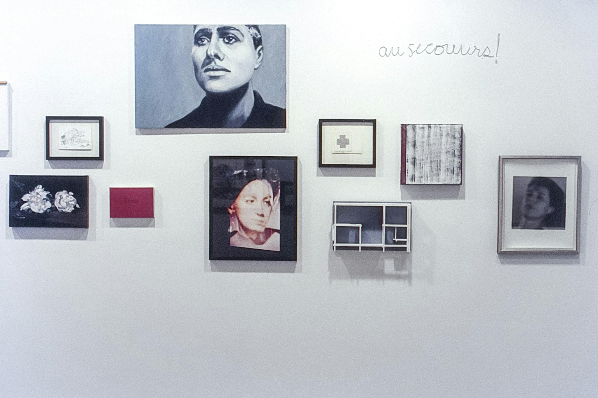 Eleven artworks mounted on a white wall. The works include a small all-red painting, a double exposure photo portrait, and a text work that reads "au secouirs!". Some works are framed, some are not.