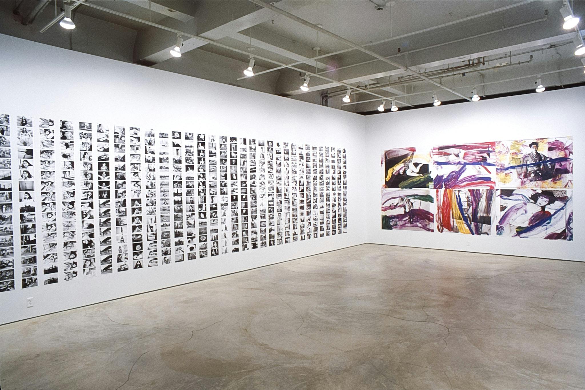 Two gallery walls are filled with black and white photographs. The left wall is covered by small photographs aligned in vertical rows. Six large ones, with some paints on, are on the other wall. 